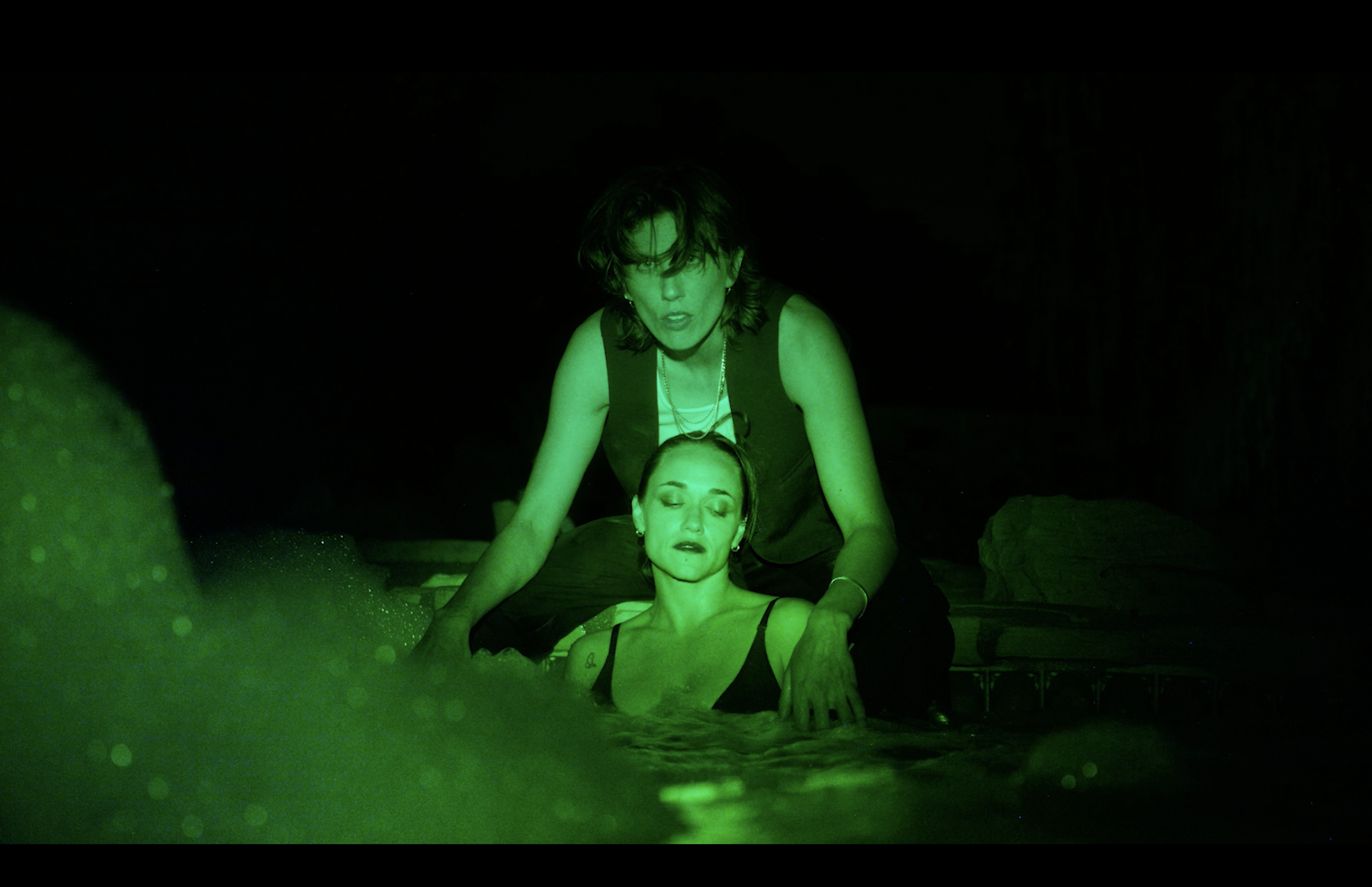 A woman with dark hair receiving a massage or treatment in a dark, green-lit environment, with her eyes closed and a calm expression.
