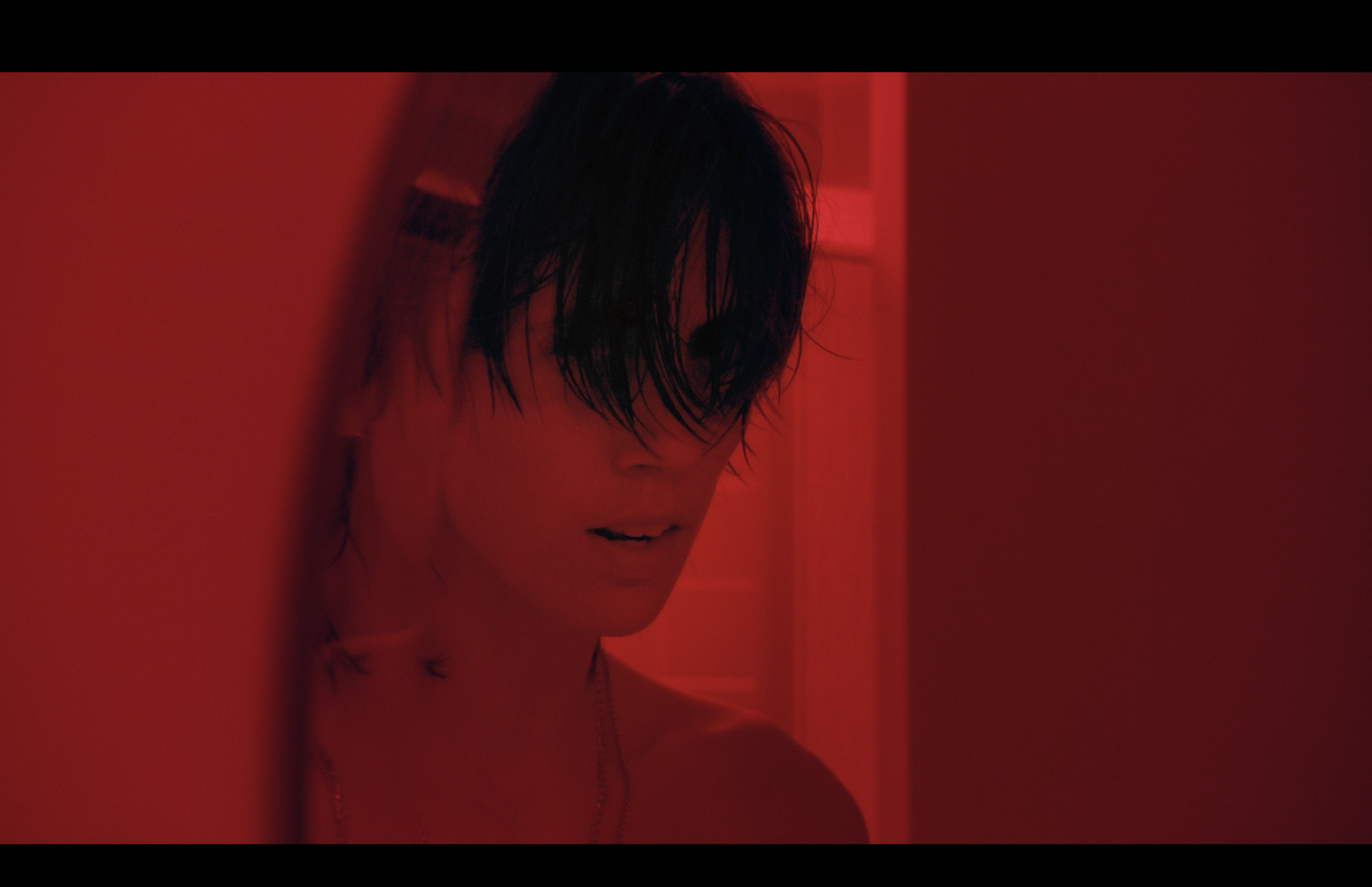 A person with wet hair and minimal clothing, illuminated by red lighting, creating a moody and artistic atmosphere.