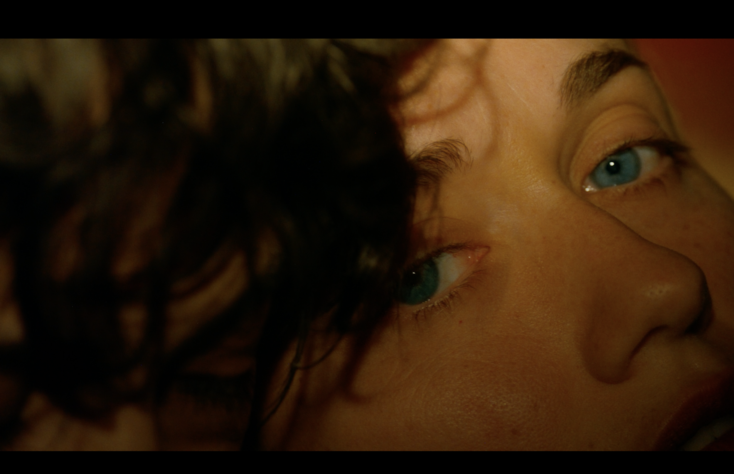 Close-up of a person's eye with blue irises, partially obscured by dark hair.