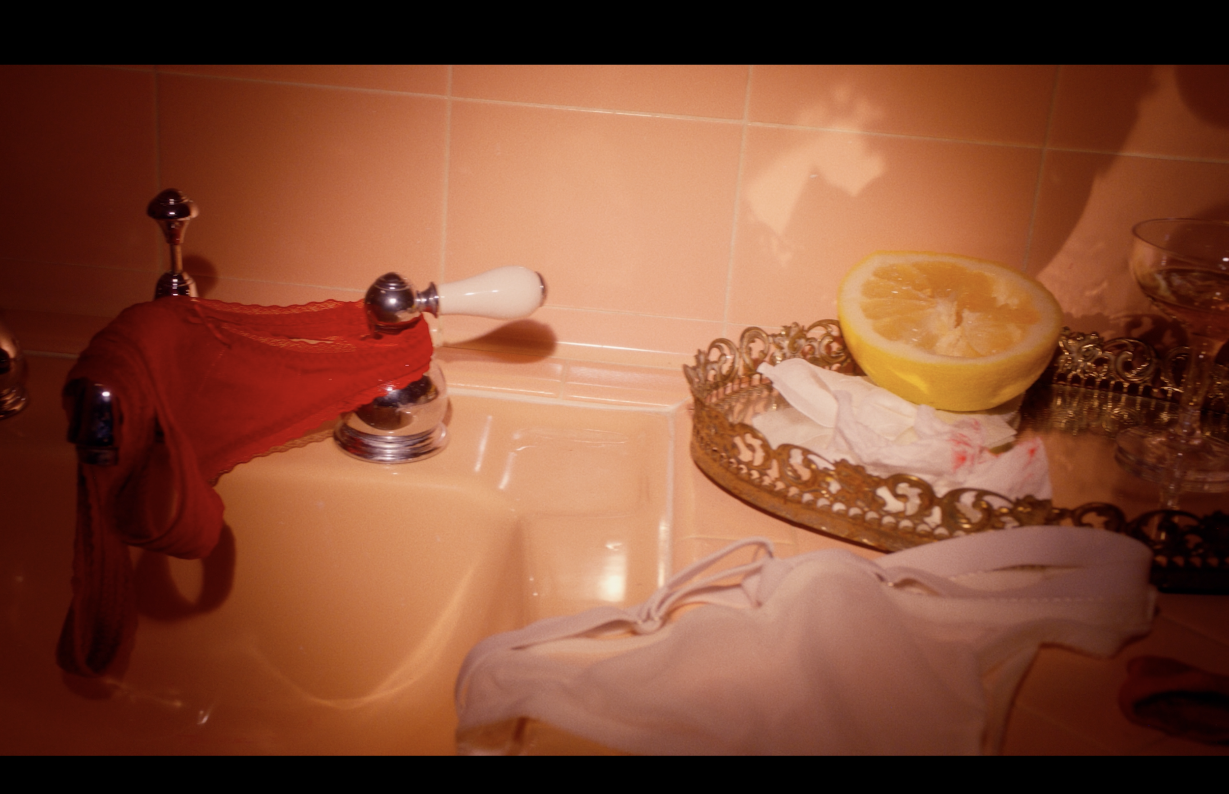 A sink with orange tiles, a red cloth, a white soap dispenser, a decorative tray with a half-cut lemon, a glass, and a tissue.