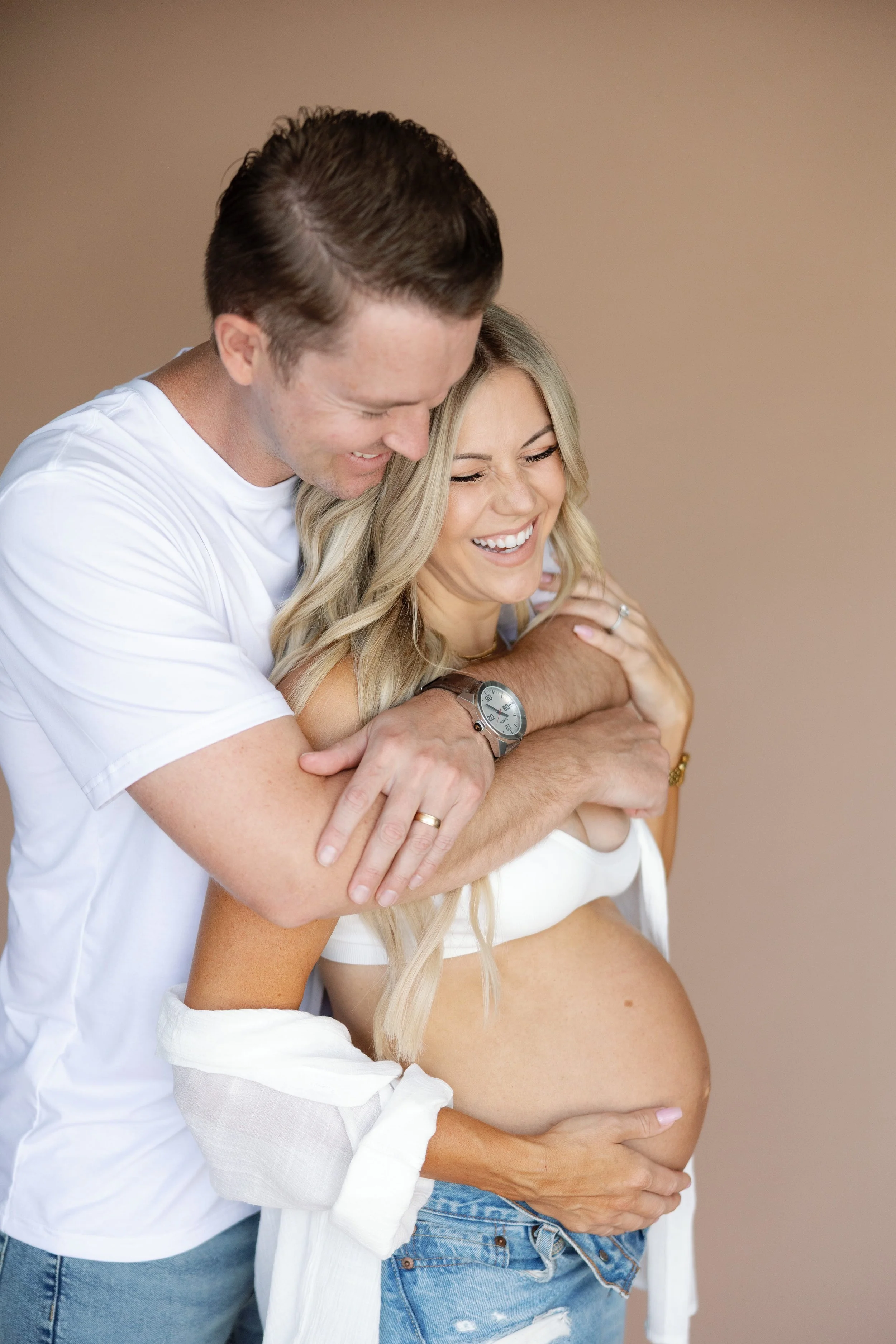 Couple smiles holding baby bump during maternity photo session in a studio