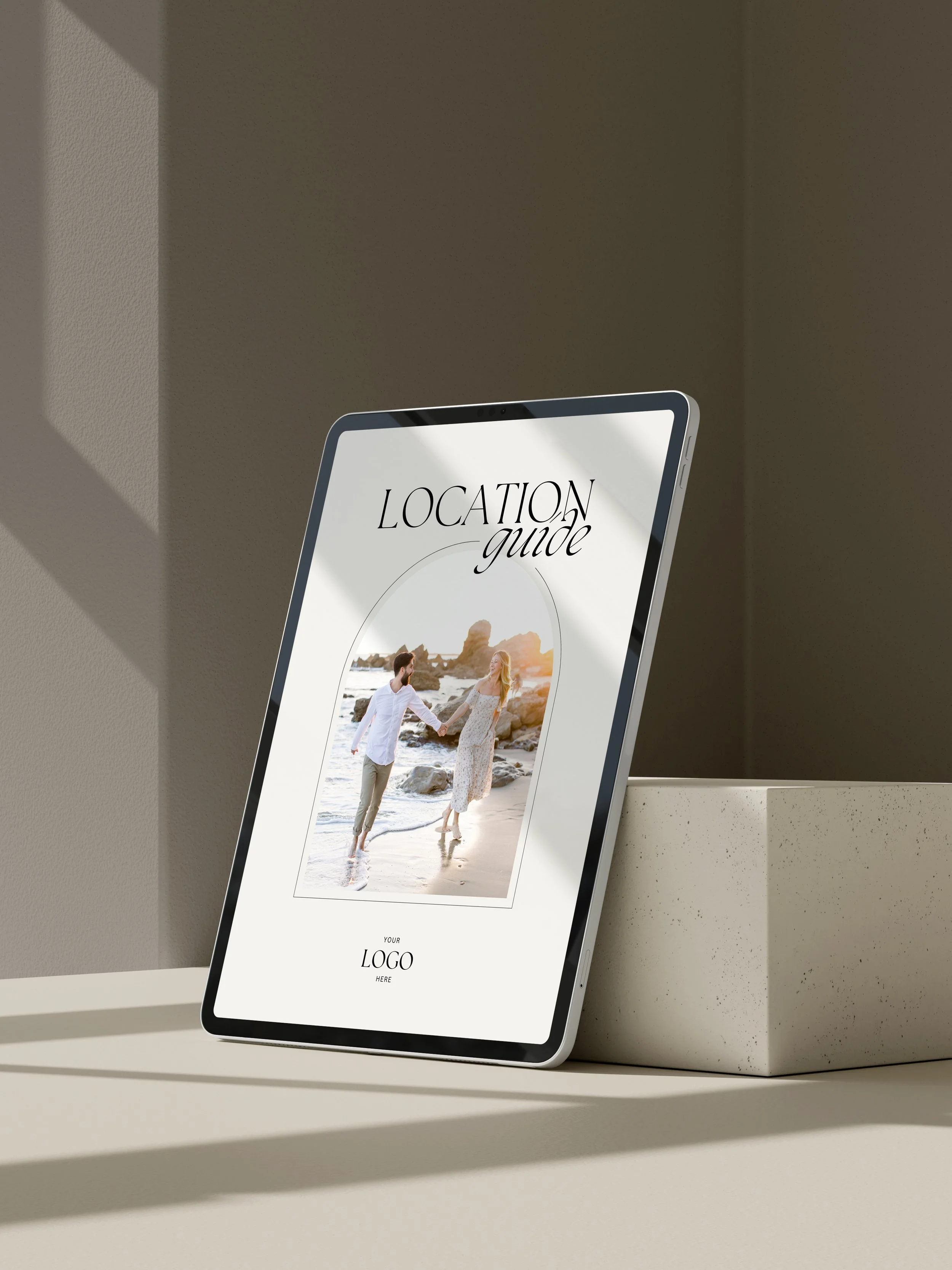 A tablet displaying a photo of a couple holding hands on the beach with rocky formations in the background and the text 'Location Guide' at the top.