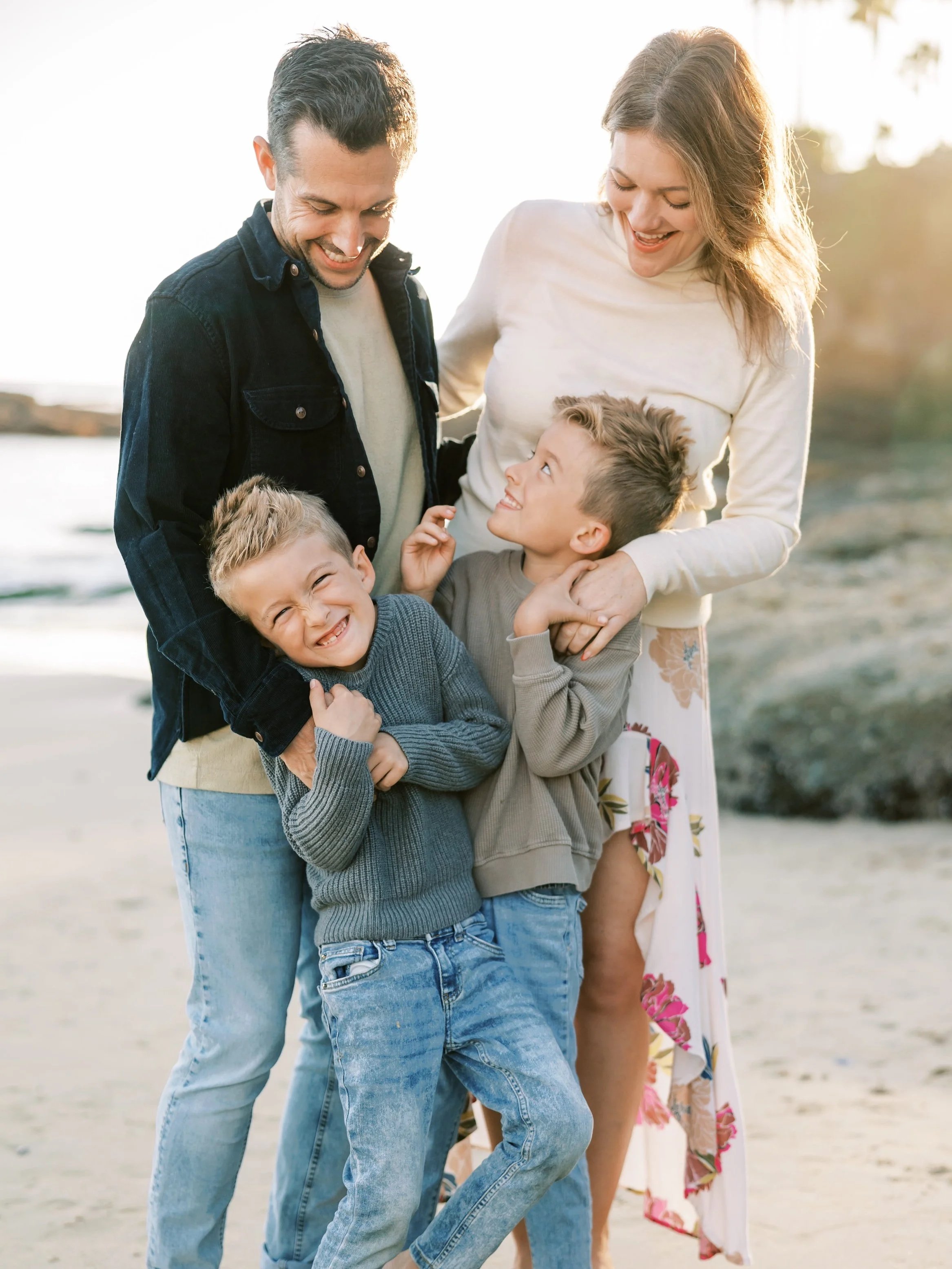 A happy family of four, consisting of two adults and two children, enjoying time together on the beach during sunset.