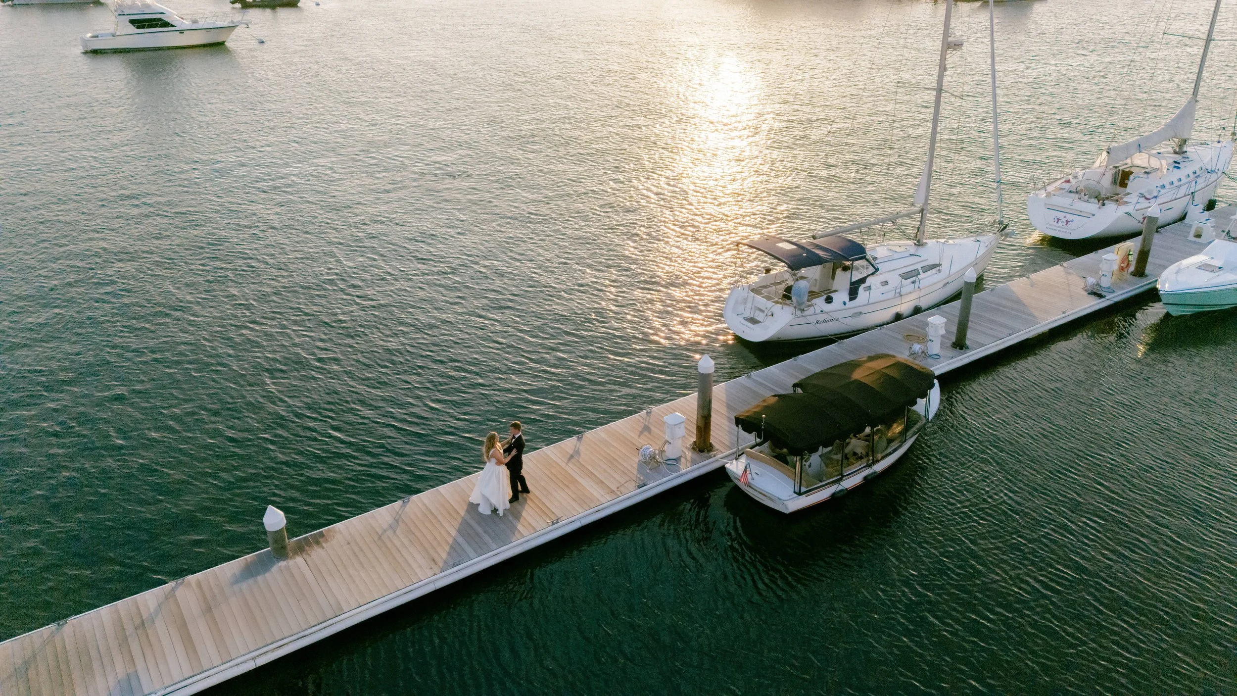 Bride & Groom take photos on the dock at the Balboa Yacht Club with a sailboat in the background during their Newport Beach Wedding