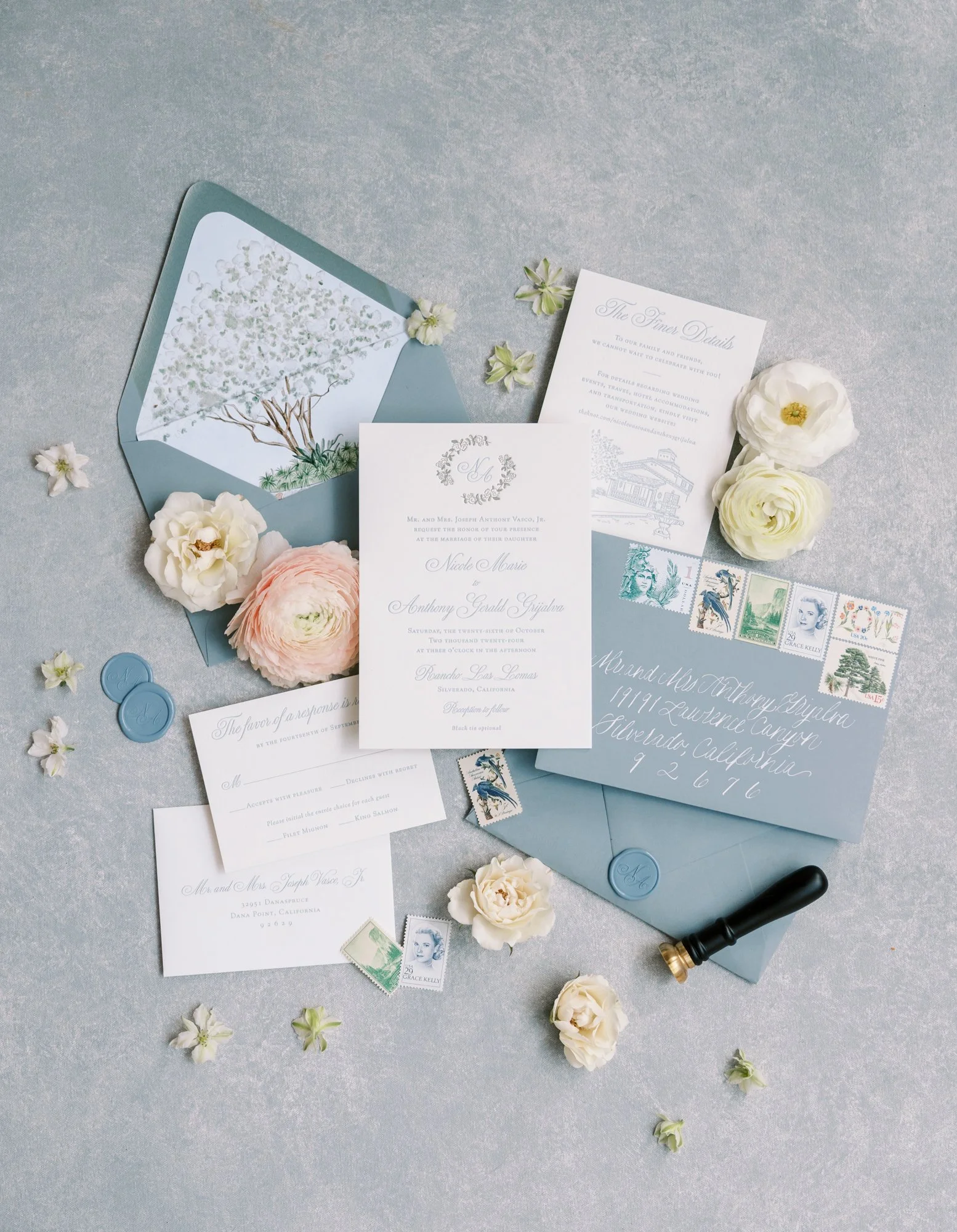 Wedding invitation suite with floral accents, stamps, and a light blue envelope on a silver textured background.