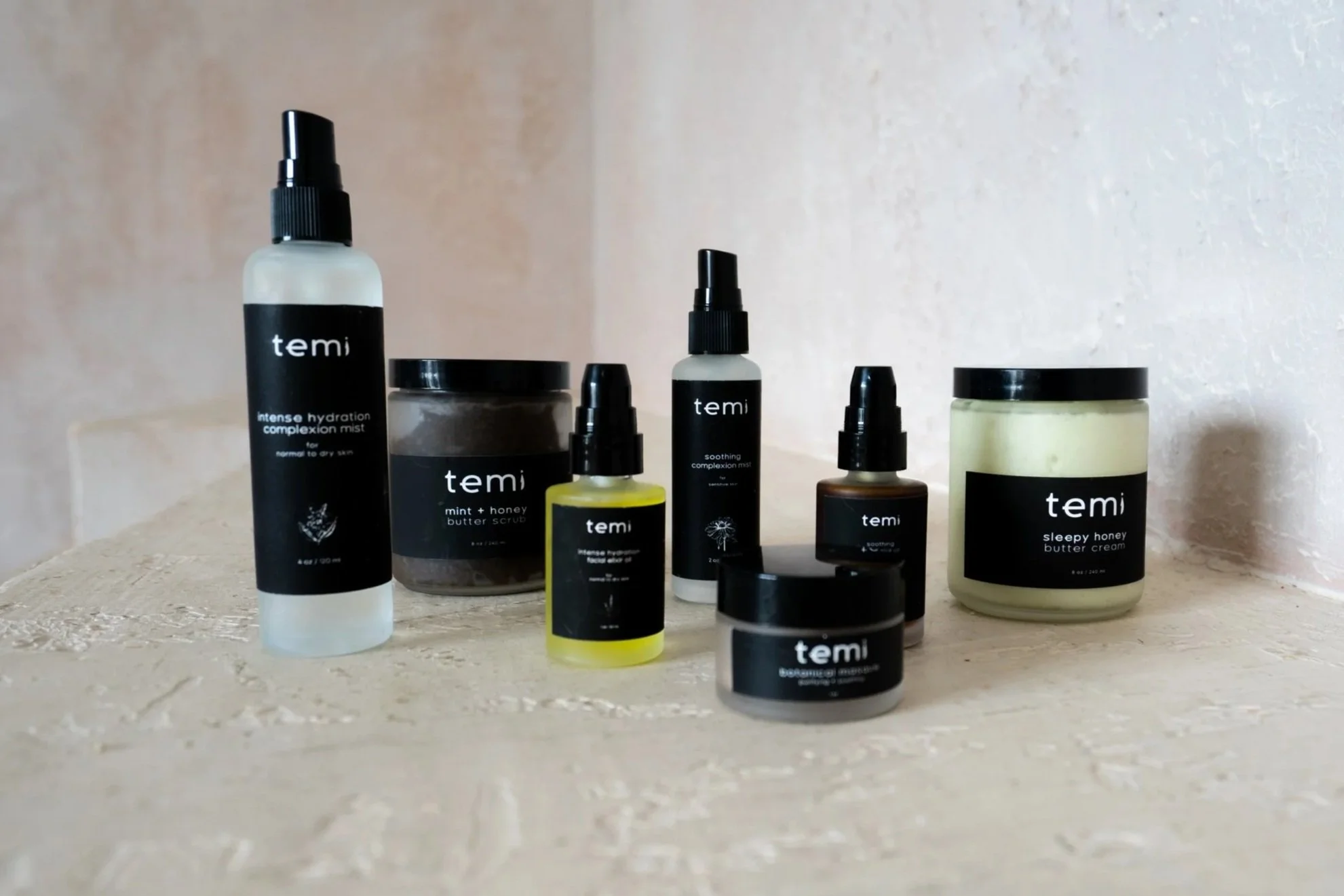 Collection of skincare products in black and yellow containers, including creams, serums, scrubs, and mists, arranged on a textured surface.