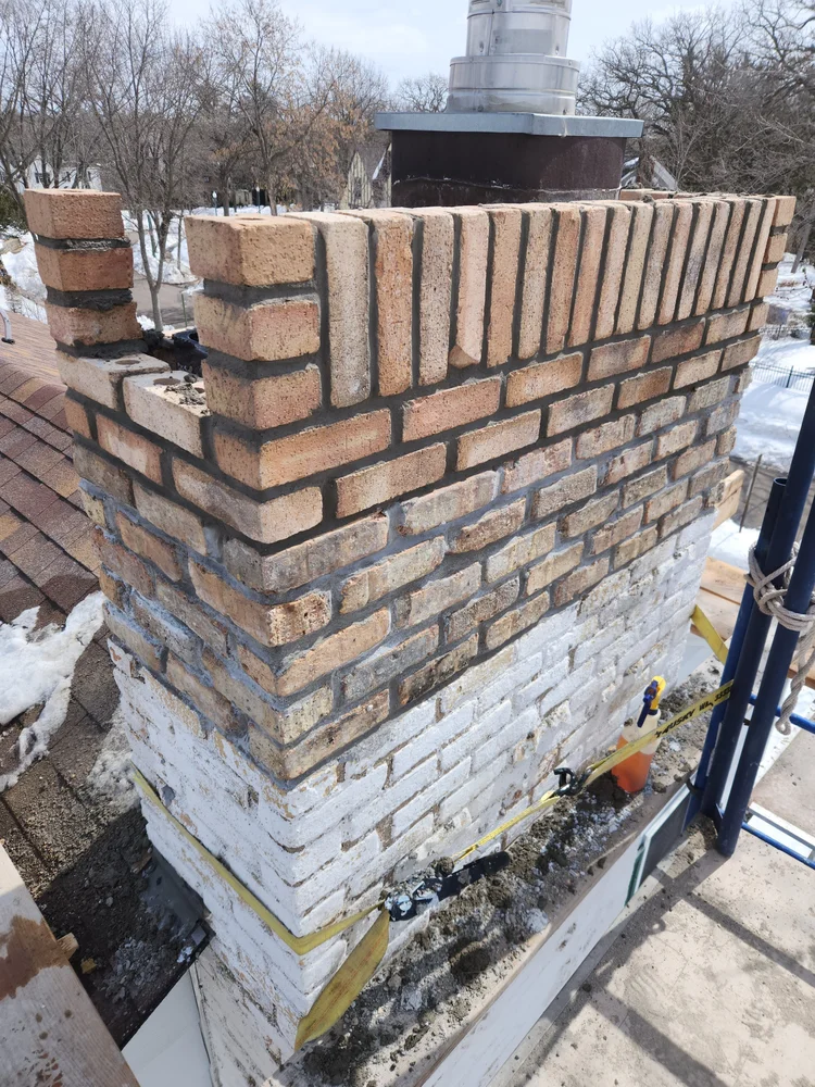 Mid-rebuild: old painted brick below, new brick going on above the roof.