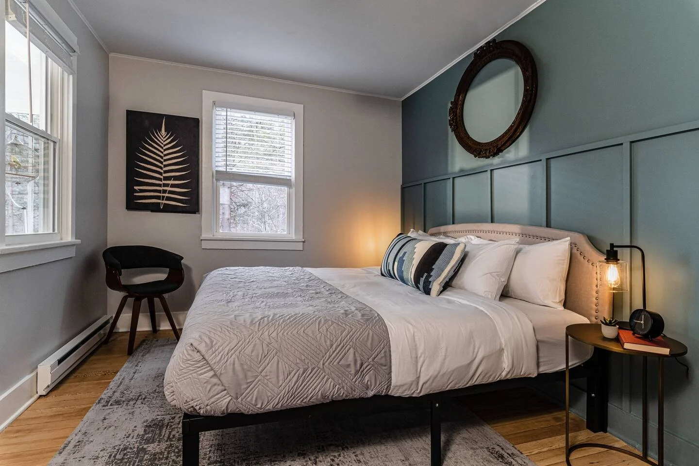 Modern bedroom with a cozy bed, decorative pillows, and a side table with a lamp and clock.