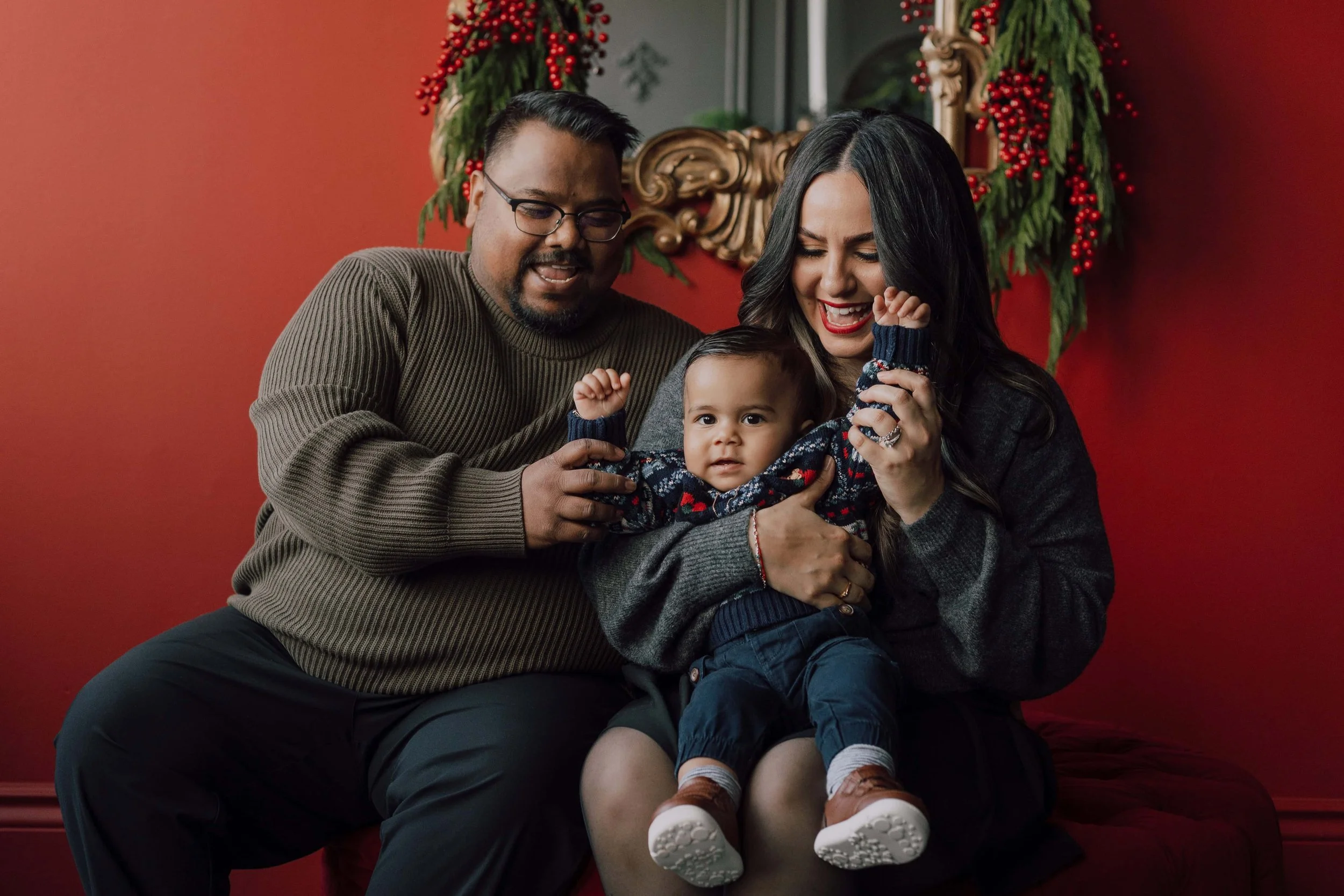 A family laughing in front of a red wall taking christmas holiday mini photography photos at Mint Room Studios