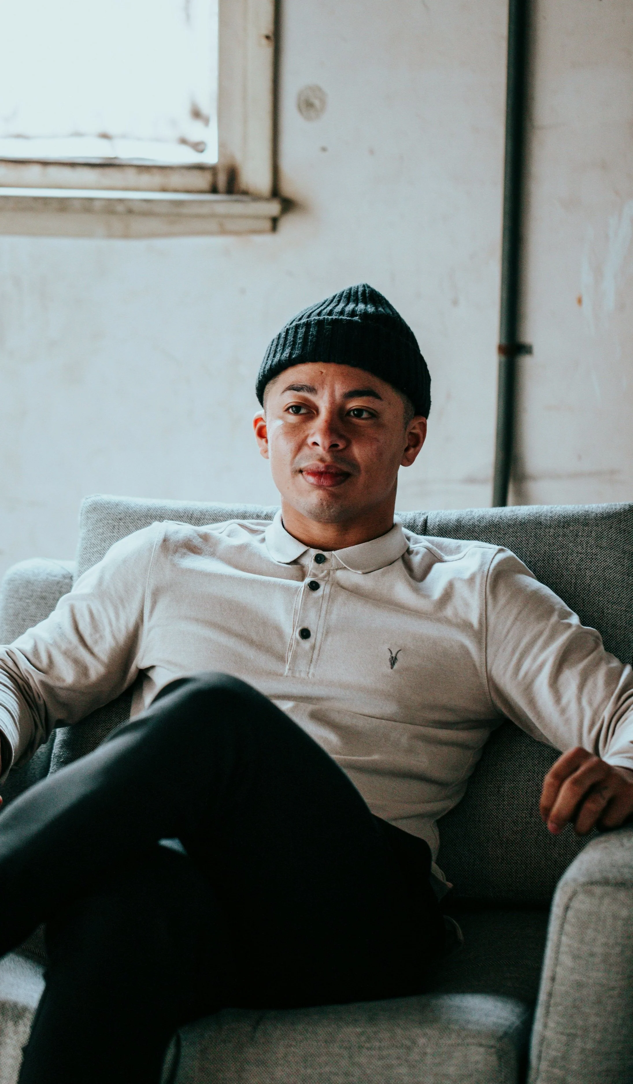 A man sits on a chair and is looking to the side, he's smiling