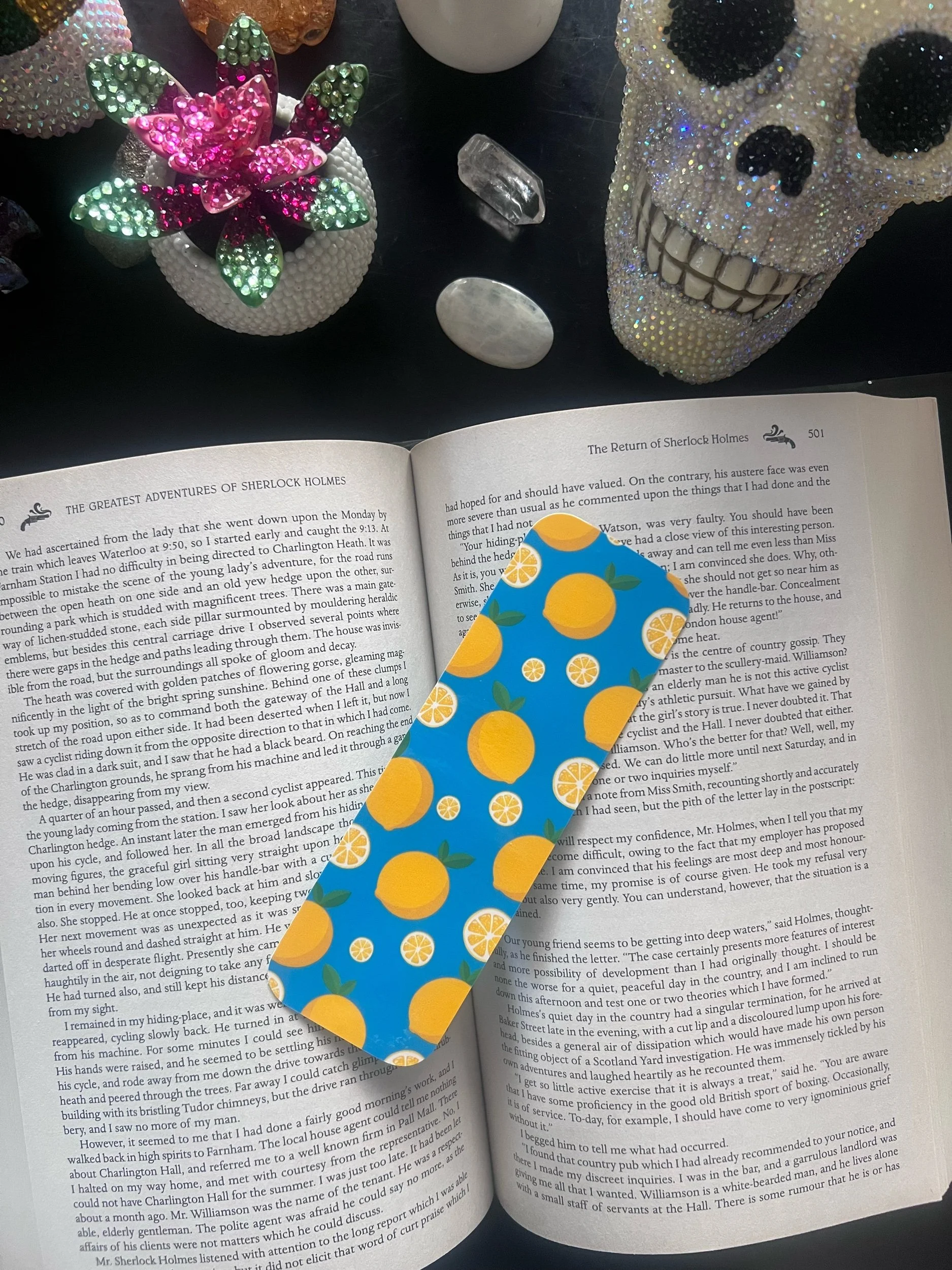 image of bookmark "lemon squeeze" on a book with a bedazeeled skull and fake plant above book, with crystals around book
