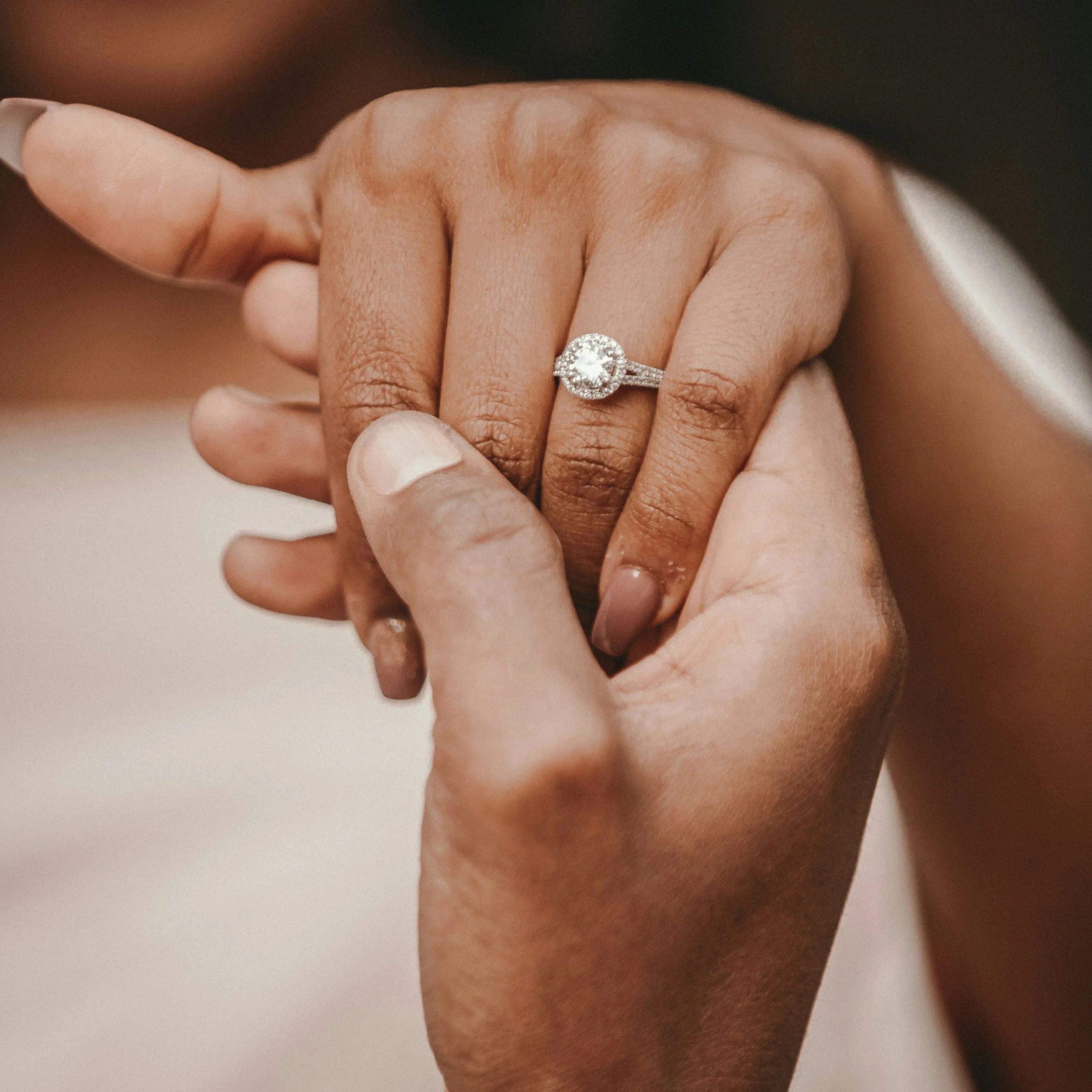 A close-up of two hands, one with a diamond engagement ring, gently holding each other.