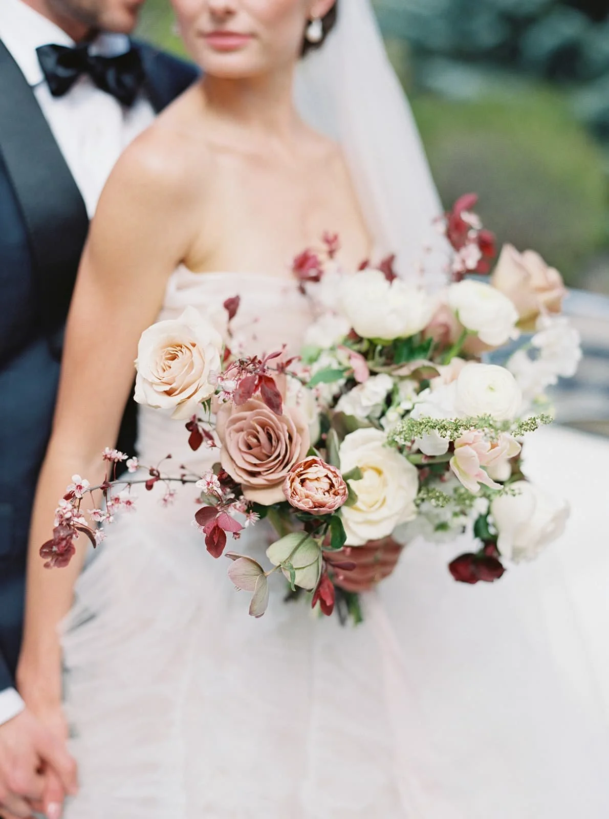 A modern bride holds a natural organic bridal bouquet designed by Twig & Bloom. The bouquet is a combination of flowering Magnolia locally sourced in BC., Roses, Ranunculus, Cherry Blossoms and Tulips in  light blush and white color palette.