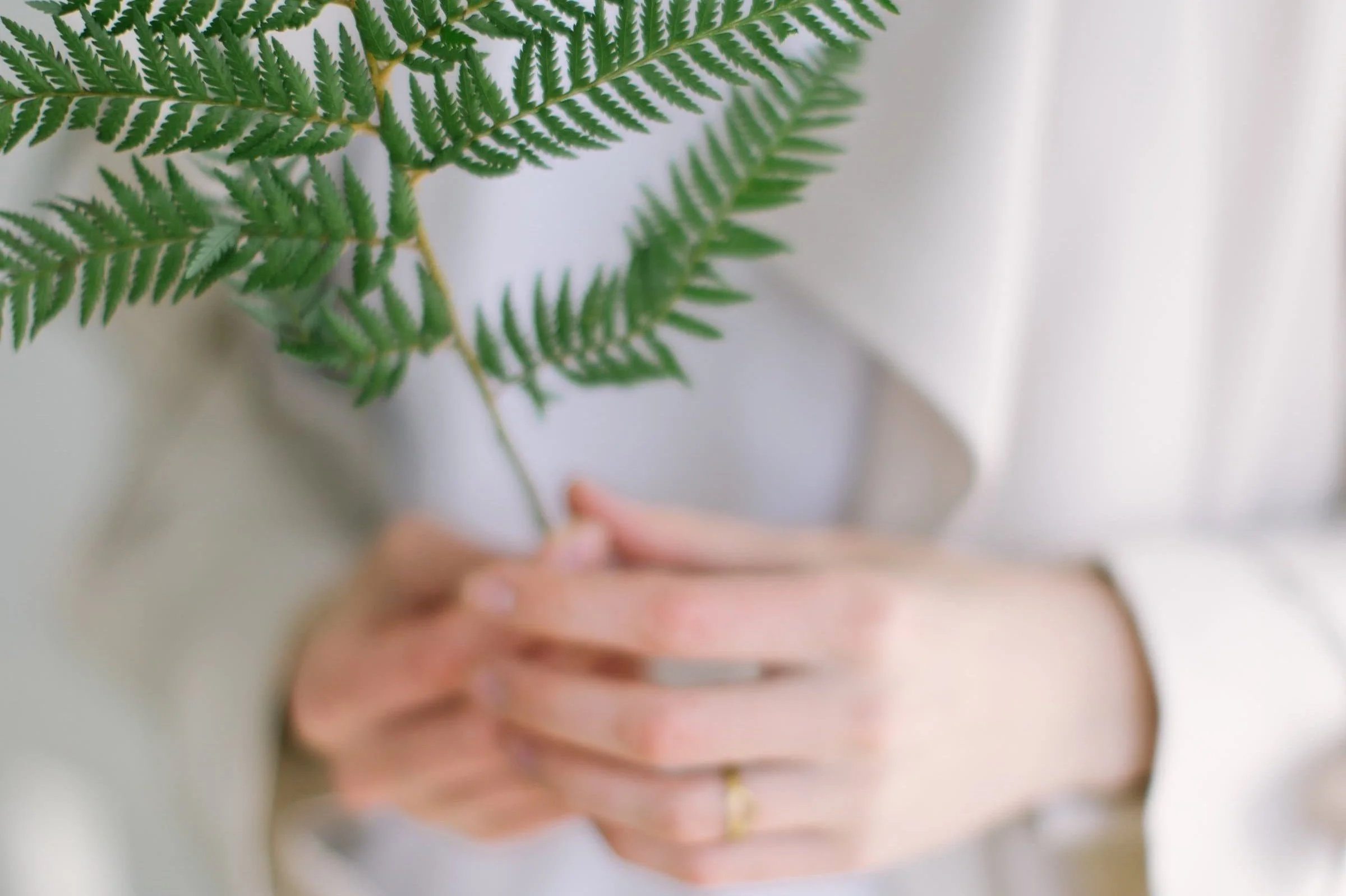 A woman holding a fern plant with both hands. The focus is on the fern and the background is blurry. It feels serene and natural.