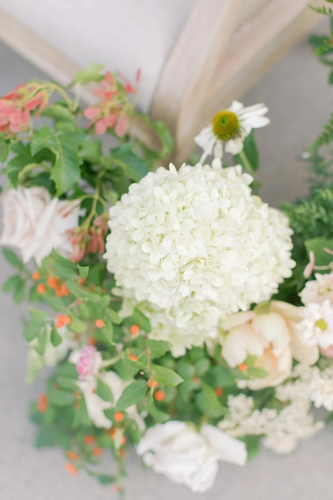 Close-up of a bouquet of white hydrangeas, a white daisy with a yellow center, green leaves, and small pink and orange flowers.