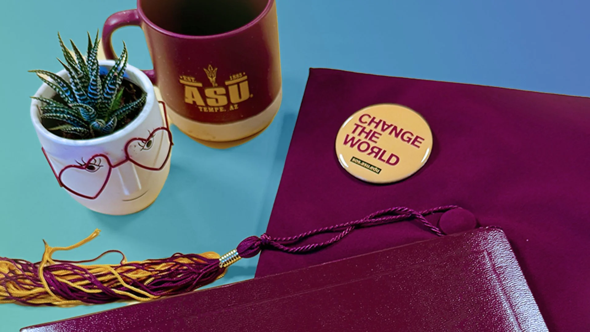 A table with two coffee mugs, one featuring a unicorn design, and a small potted succulent plant. A purple folder or gift bag with a yellow sticker reading 'CHANGE THE WORLD' is also on the table.