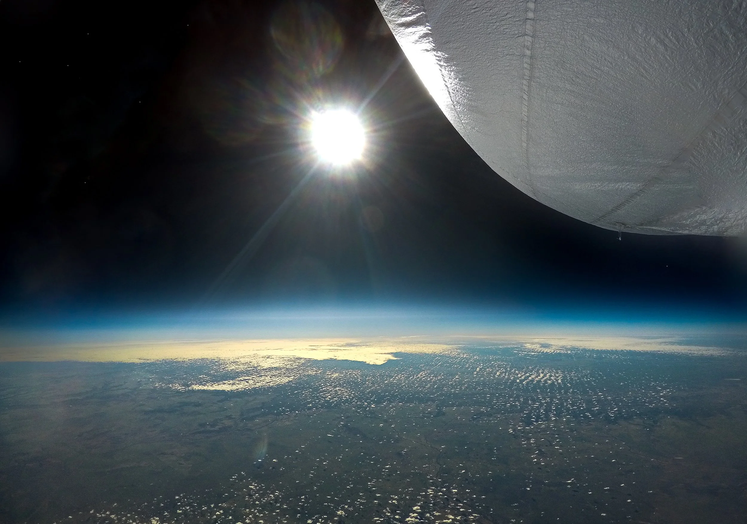 View of the Earth's atmosphere from the stratosphere with the sun shining brightly and a Stratoship partially visible in the upper right corner.