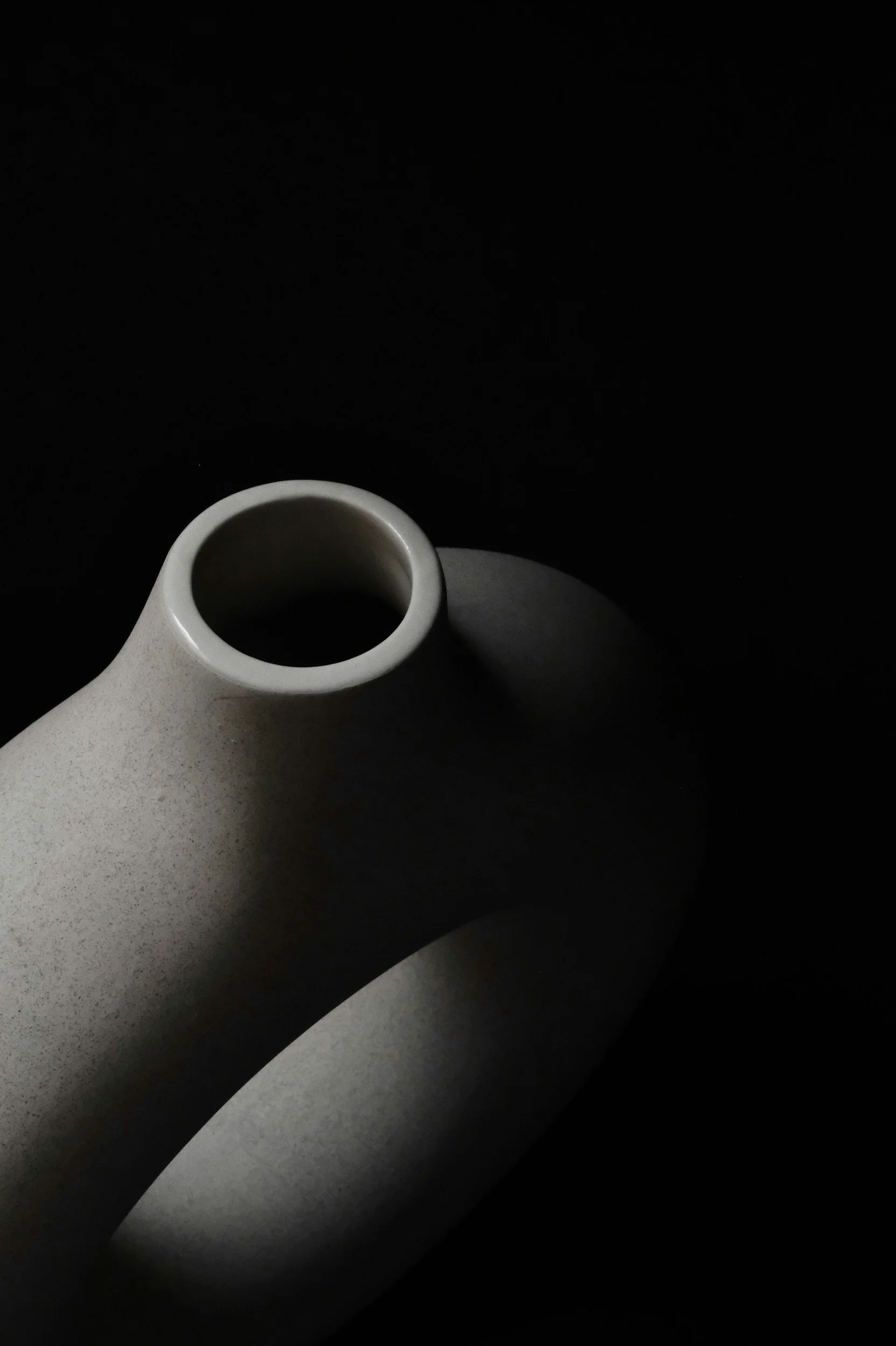 Close-up of a white ceramic vase against a black background, with minimal lighting casting shadows.