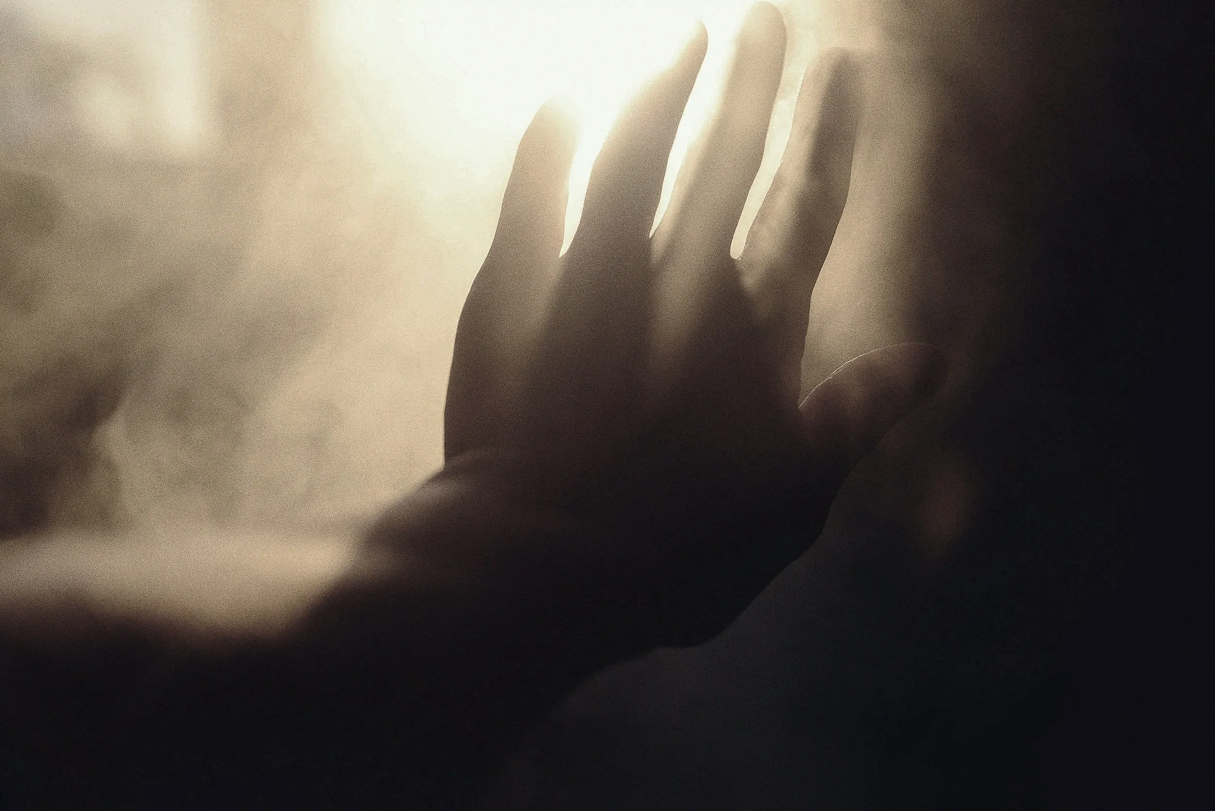 A silhouette of a hand reaching out towards bright light, with soft shadows and a warm glow.
