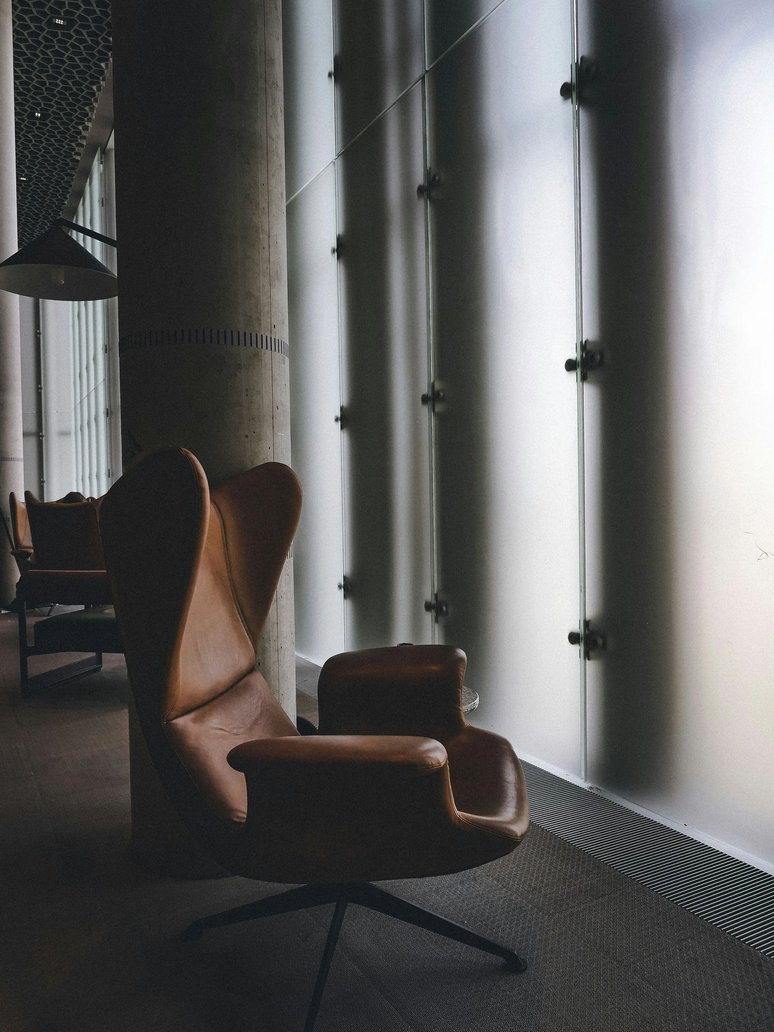 A brown leather armchair near large glass windows in a modern interior space.