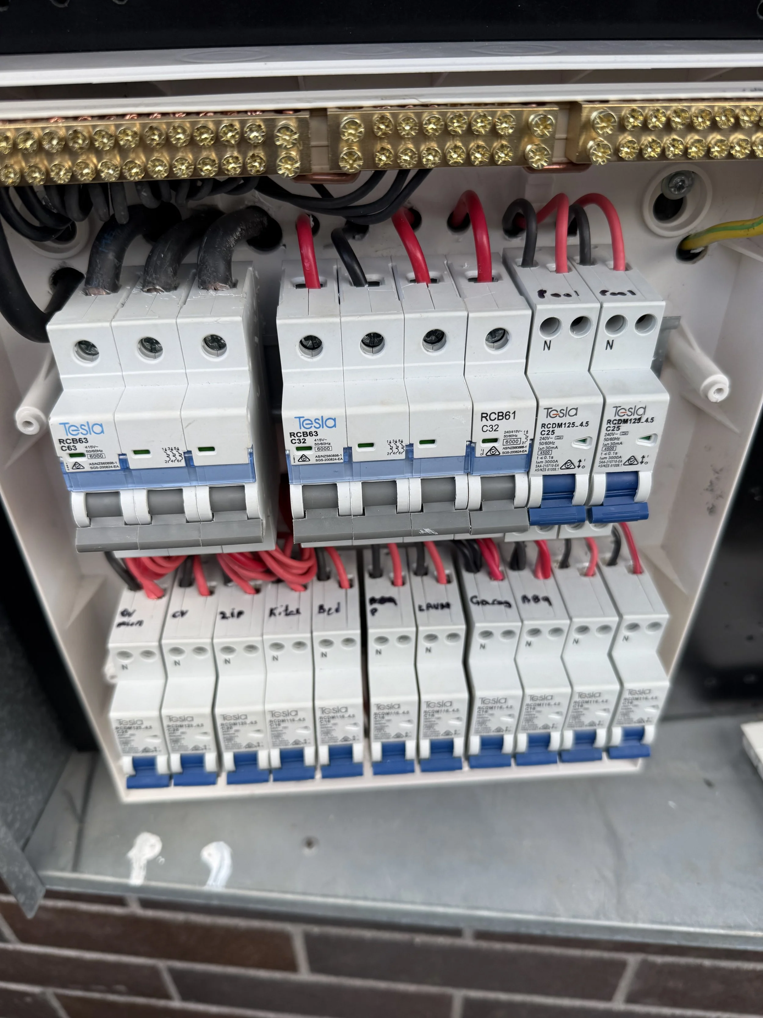 An electrical circuit breaker panel containing multiple circuit breakers, including Tesla and RCB brands, with wires connected to each breaker.