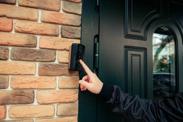 A person pressing a doorbell button on a brick wall next to a black door.