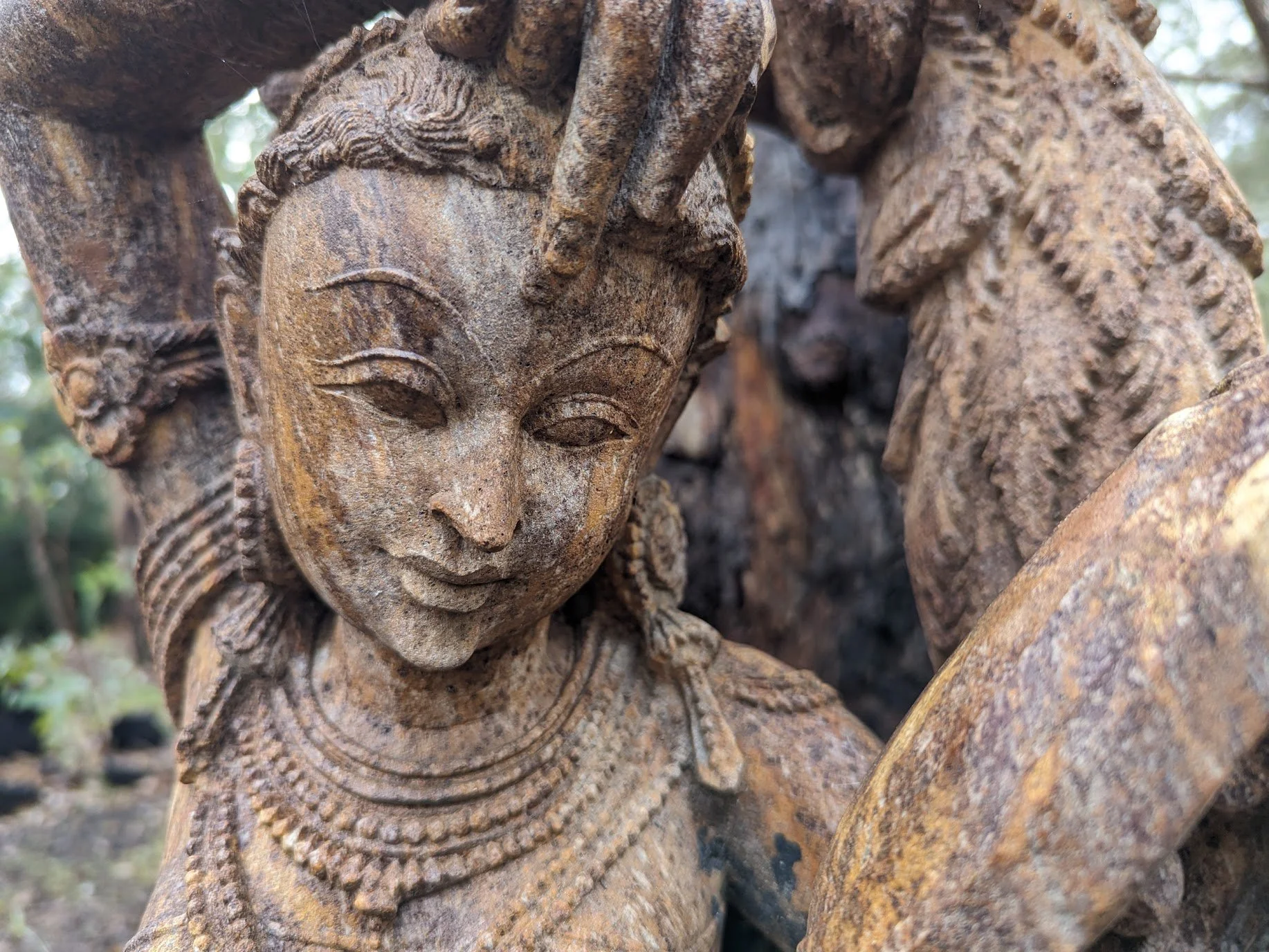 Close-up of an intricate stone sculpture of a woman with detailed jewelry and hair, shown outdoors.