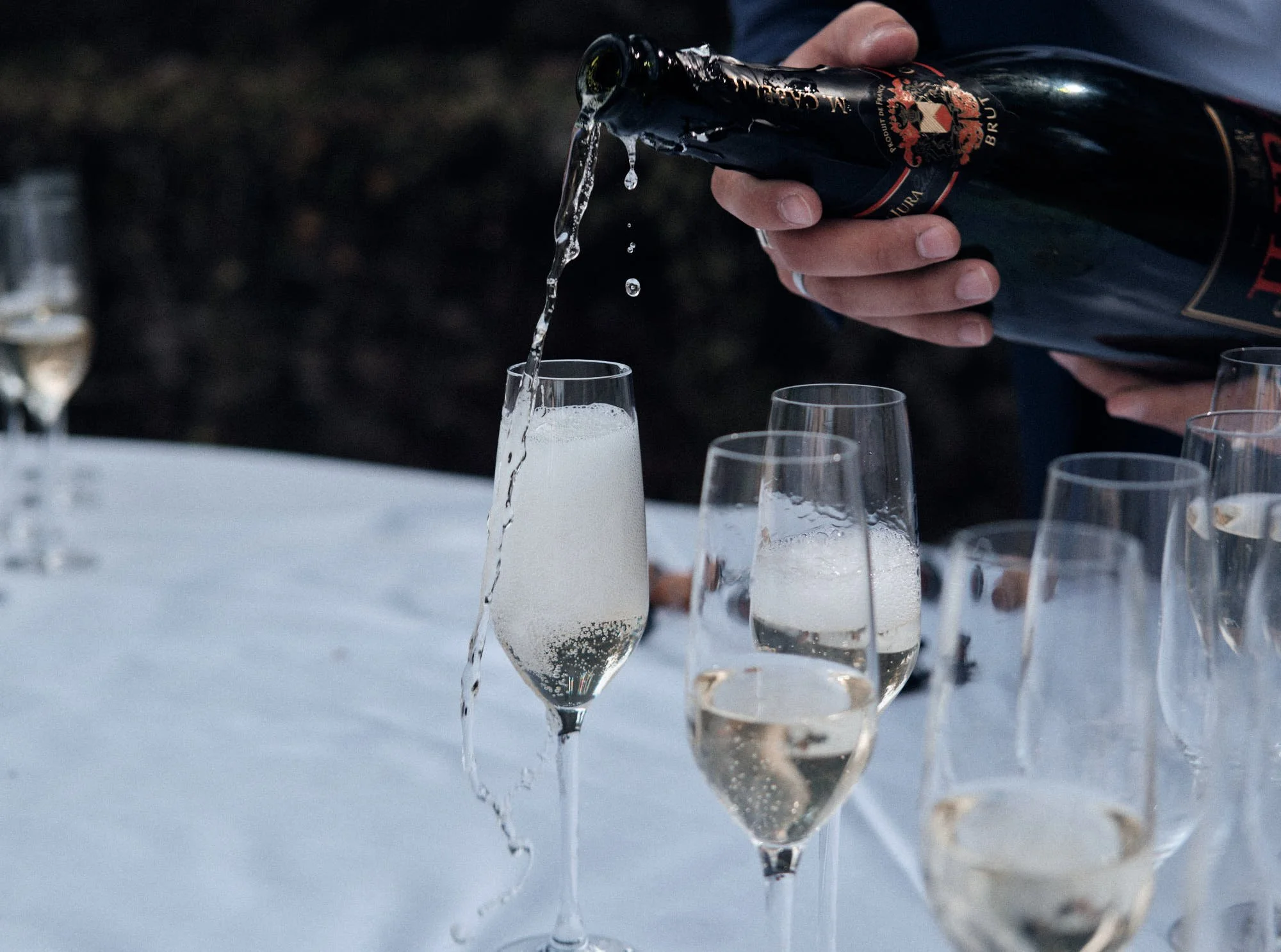 Lors d'un mariage dans le Jura une personne verse du champagne dans une flûte lors d'une fête, plusieurs autres verres sont visibles sur la table.