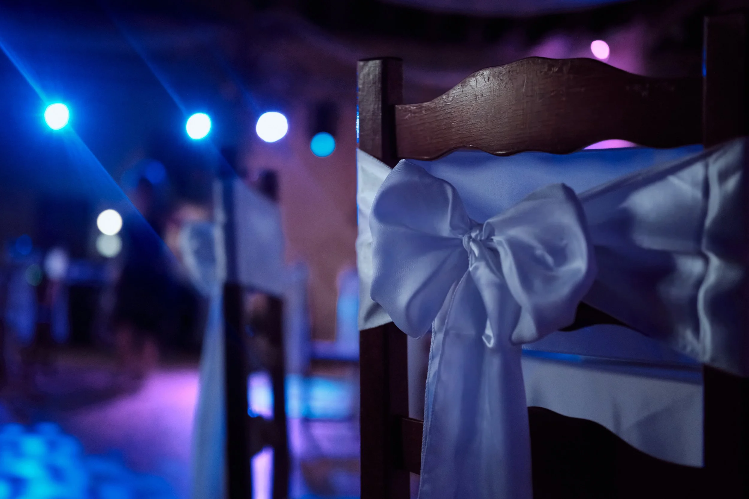 Une table en bois avec une nappe blanche pliée, dans une ambiance sombre avec des lumières colorées, semblant être une scène à un mariage dans le Jura au Château d'Artois