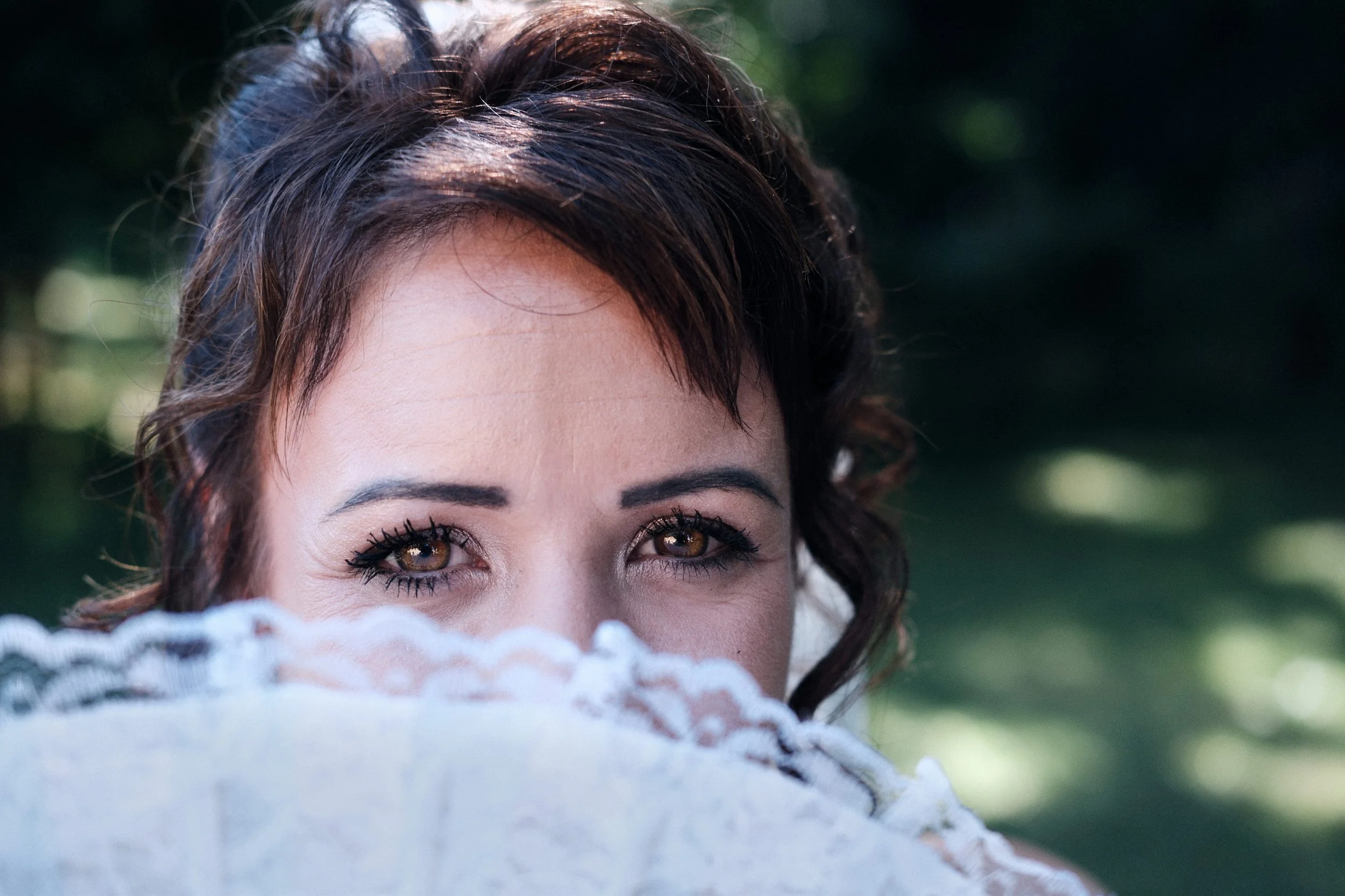 Zoom sur les yeux d'une femme mariée dans le Jura avec maquillage, en partie cachée derrière un éventail