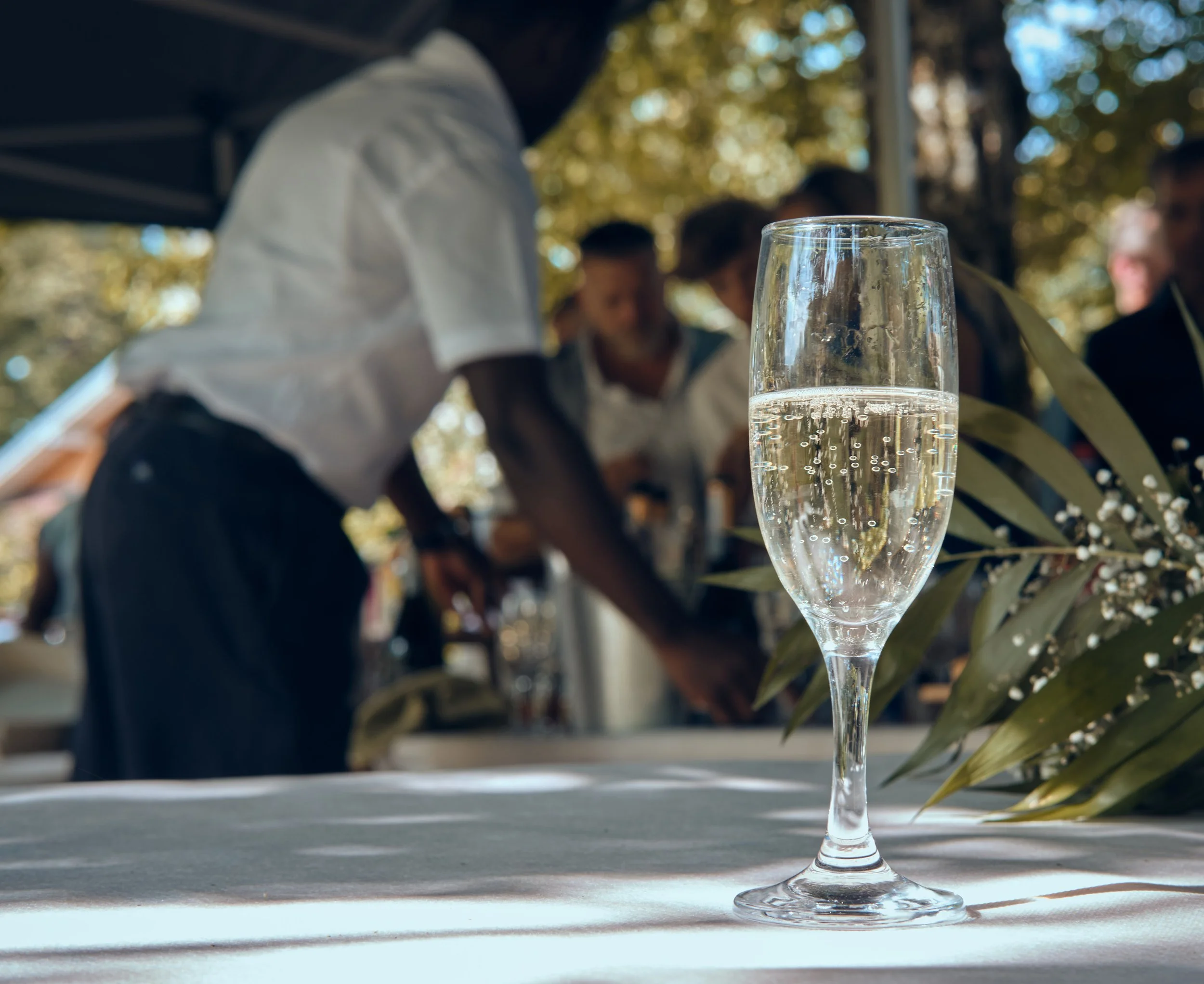 Verre de champagne à moitié plein sur une table avec des personnes floues en arrière-plan lors d'un mariage au Château d'Artois dans le Jura  en plein air par une journée ensoleillée.