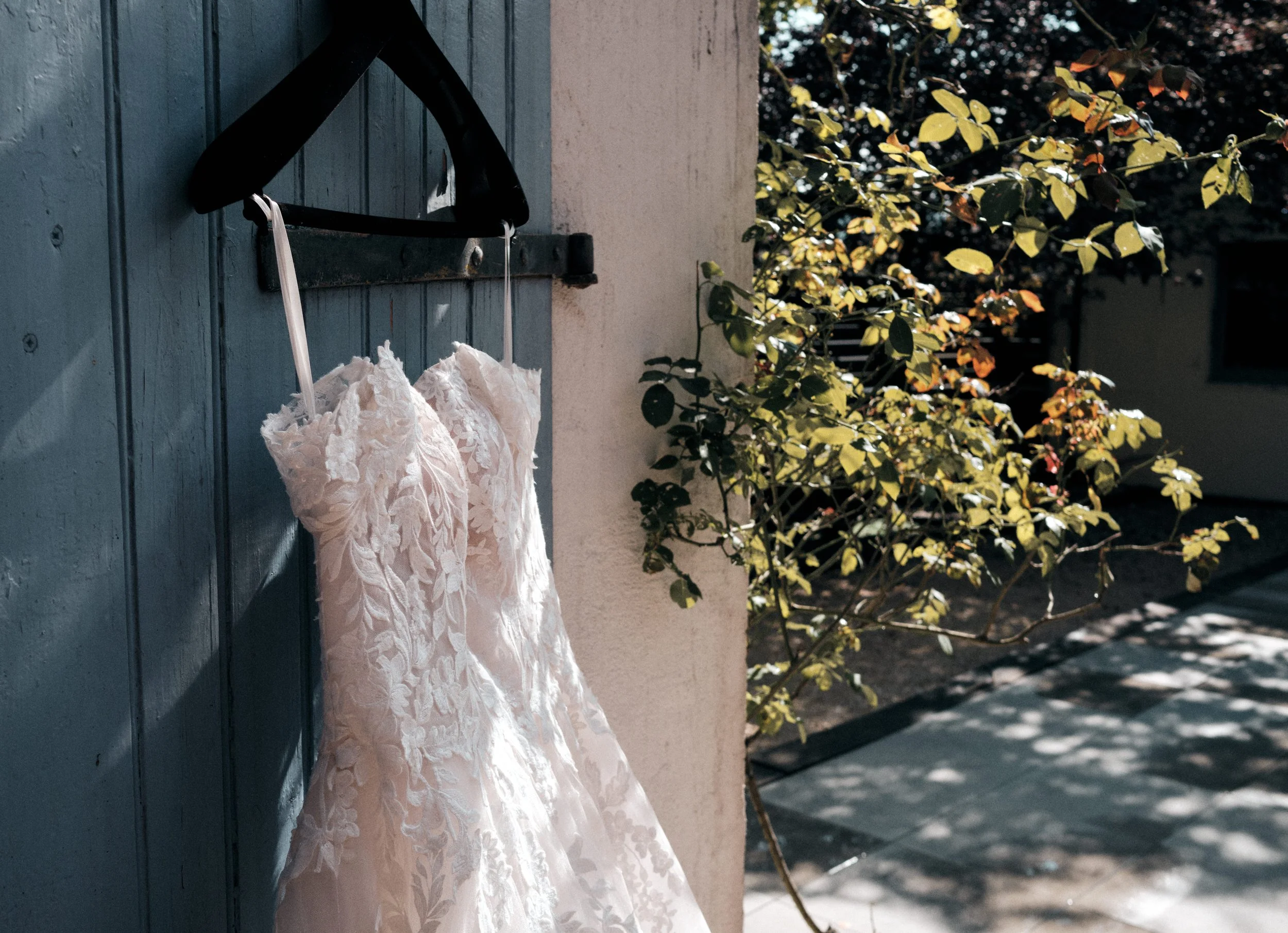 photographie d'une robe de mariée à dentelle suspendue à une porte bleu