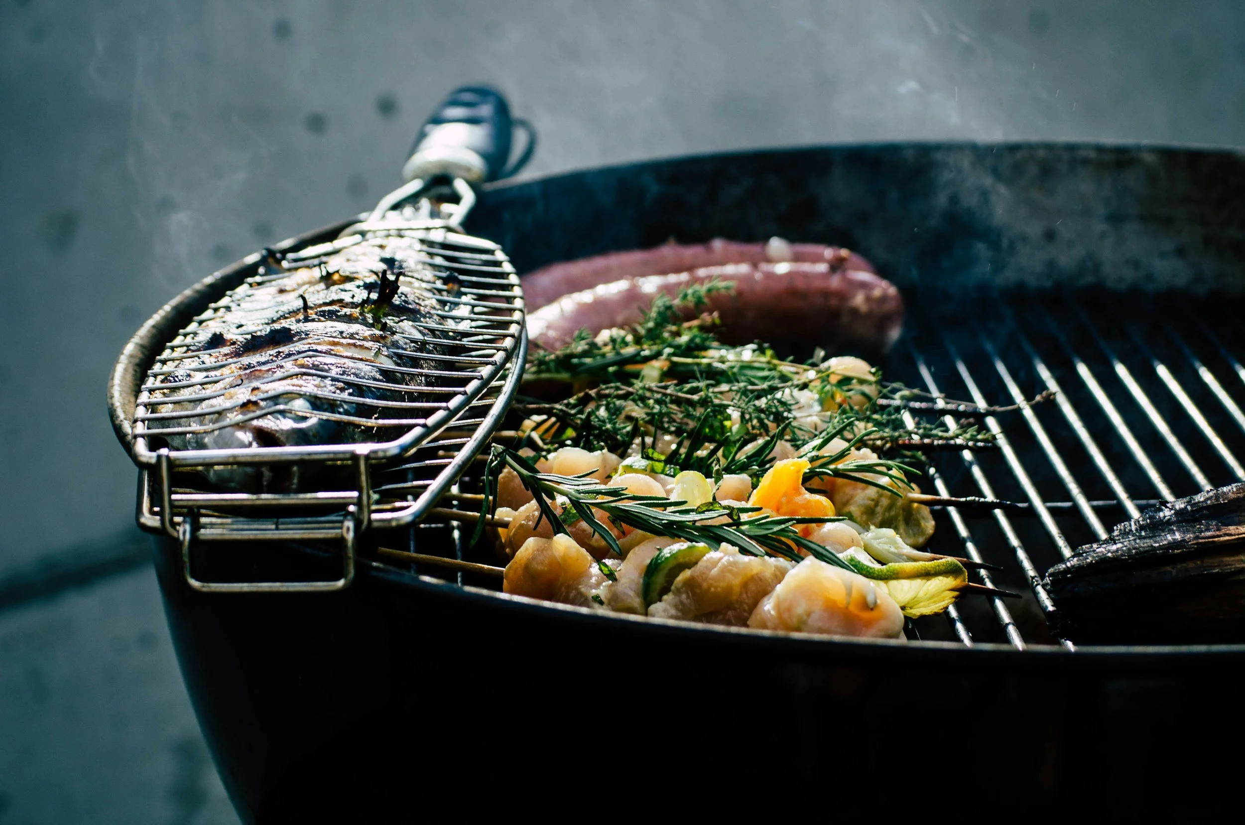 Grilled fish, sausages, chicken, and vegetables on a barbecue grill with herbs.