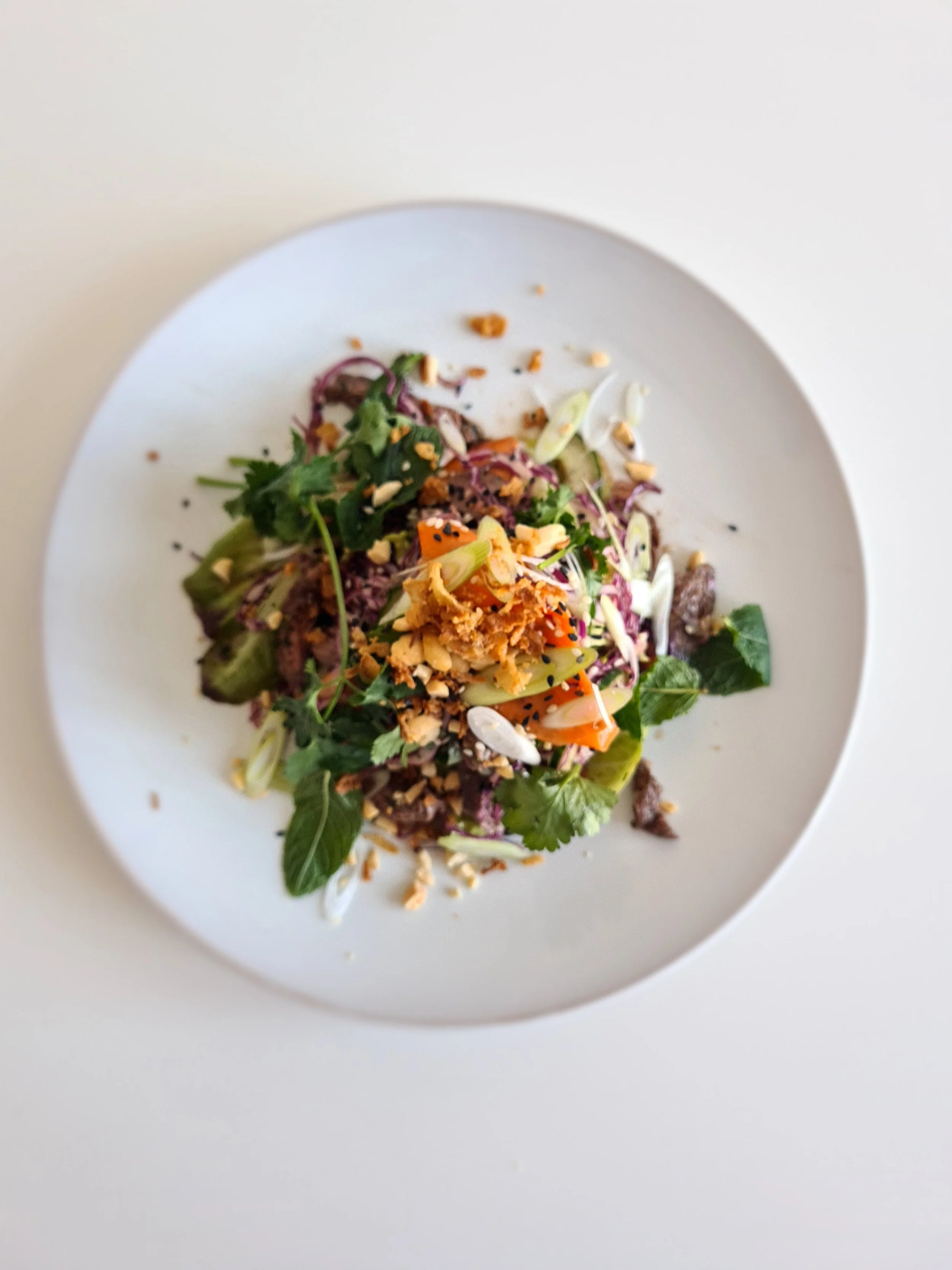 A plate of colorful mixed salad with greens, vegetables, chopped nuts, and crispy toppings on a white surface.