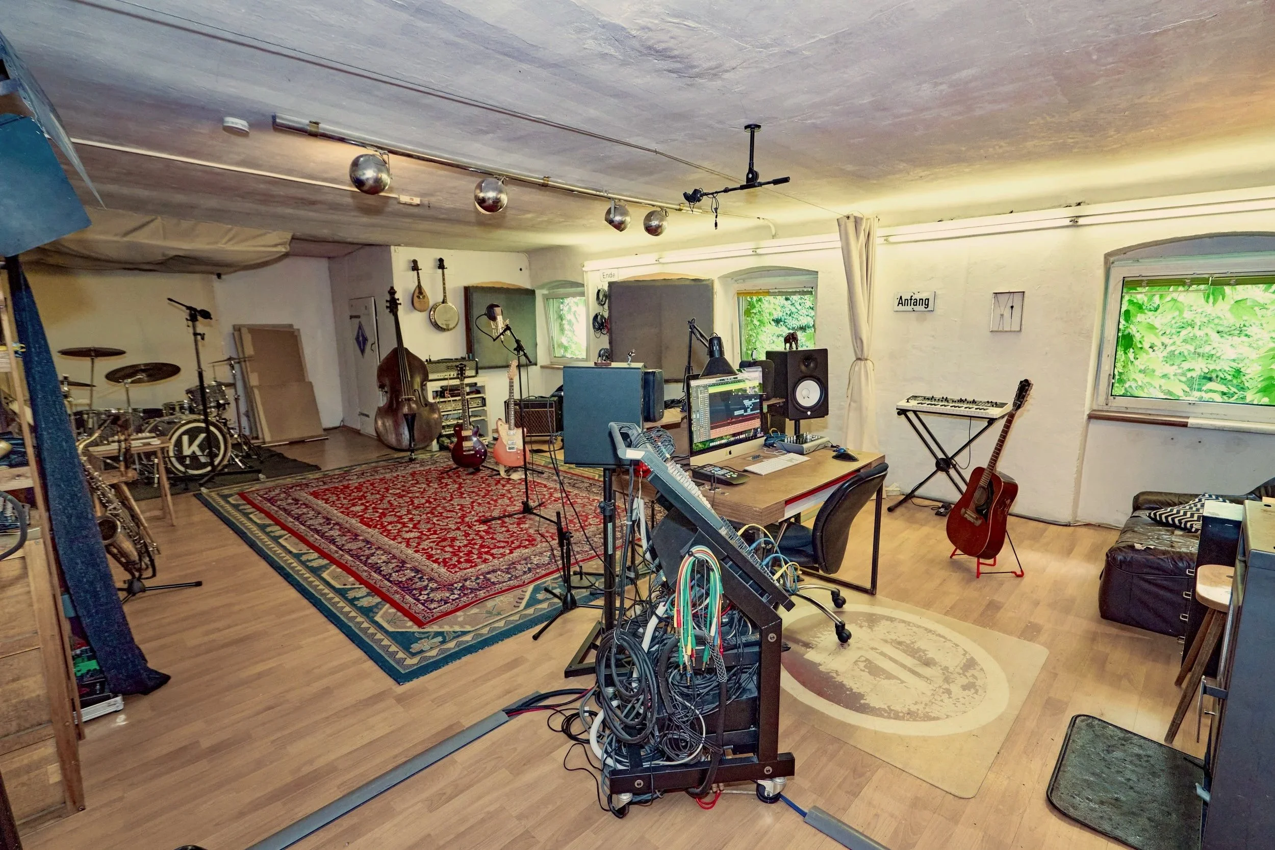 Aufnahme eines Musik- und Aufnahme-Studios mit Musikinstrumenten, Aufnahme- und Mischpulten sowie Musiksoftware am Computer. Es gibt Gitarren, ein Schlagzeug, ein Keyboard, Mikrofone und Lautsprecher. Die Atmosphäre ist kreativ und professionell.