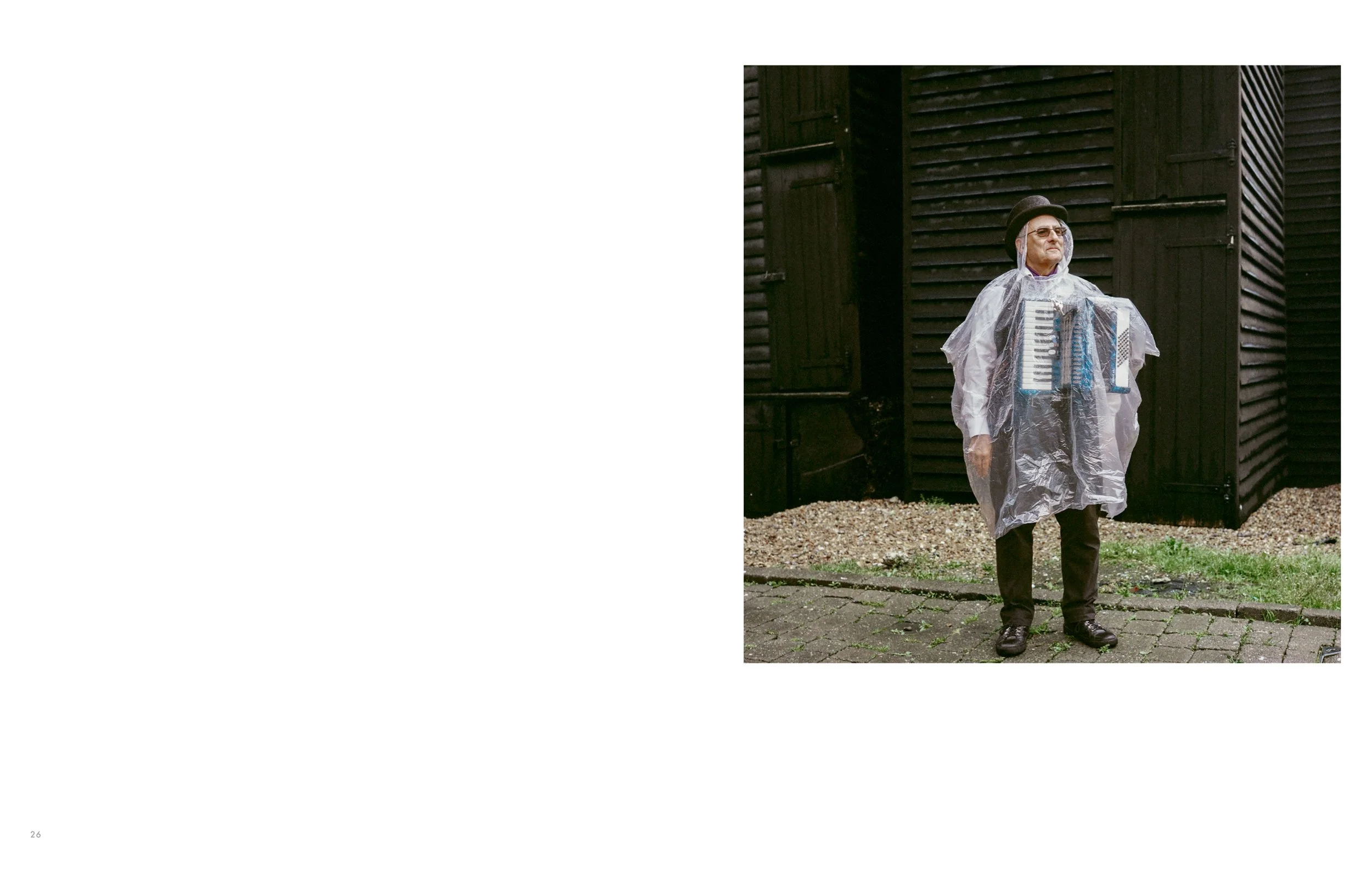 Man outdoors wearing plastic raincoat and a bowler hat, standing in front of a wooden building.
