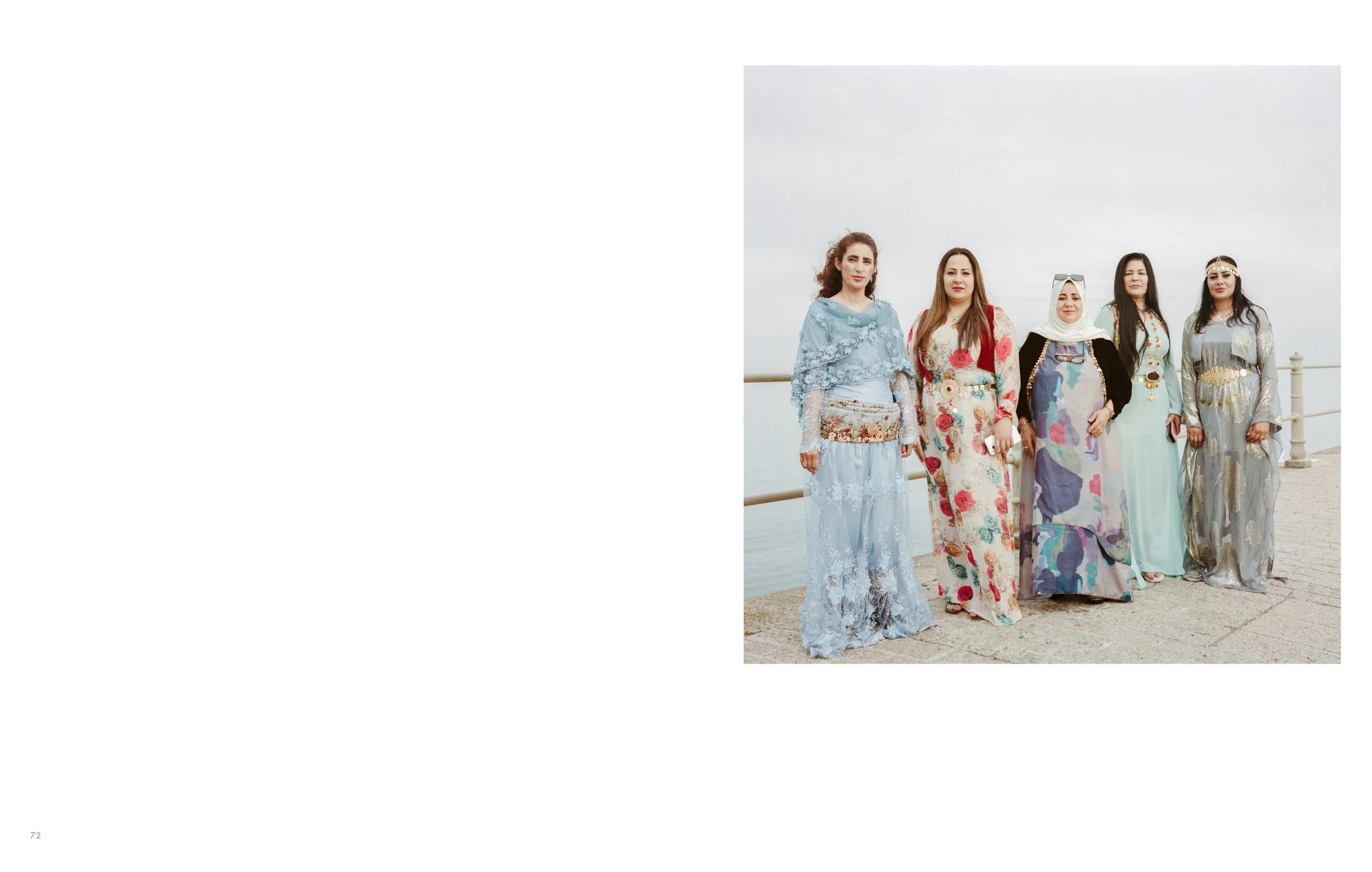 Group of women standing outdoors near water on a cloudy day, dressed in colorful long dresses.