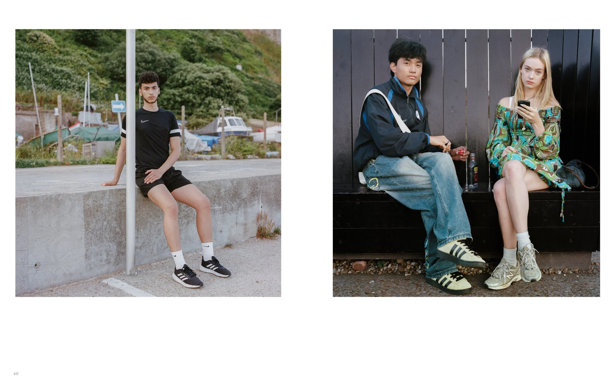 Two young adults sitting separately outdoors. The male on the left is sitting on a concrete ledge, dressed in a black t-shirt, shorts, and sneakers. The female on the right is seated on a black bench against a dark fence, wearing a colorful off-shoul