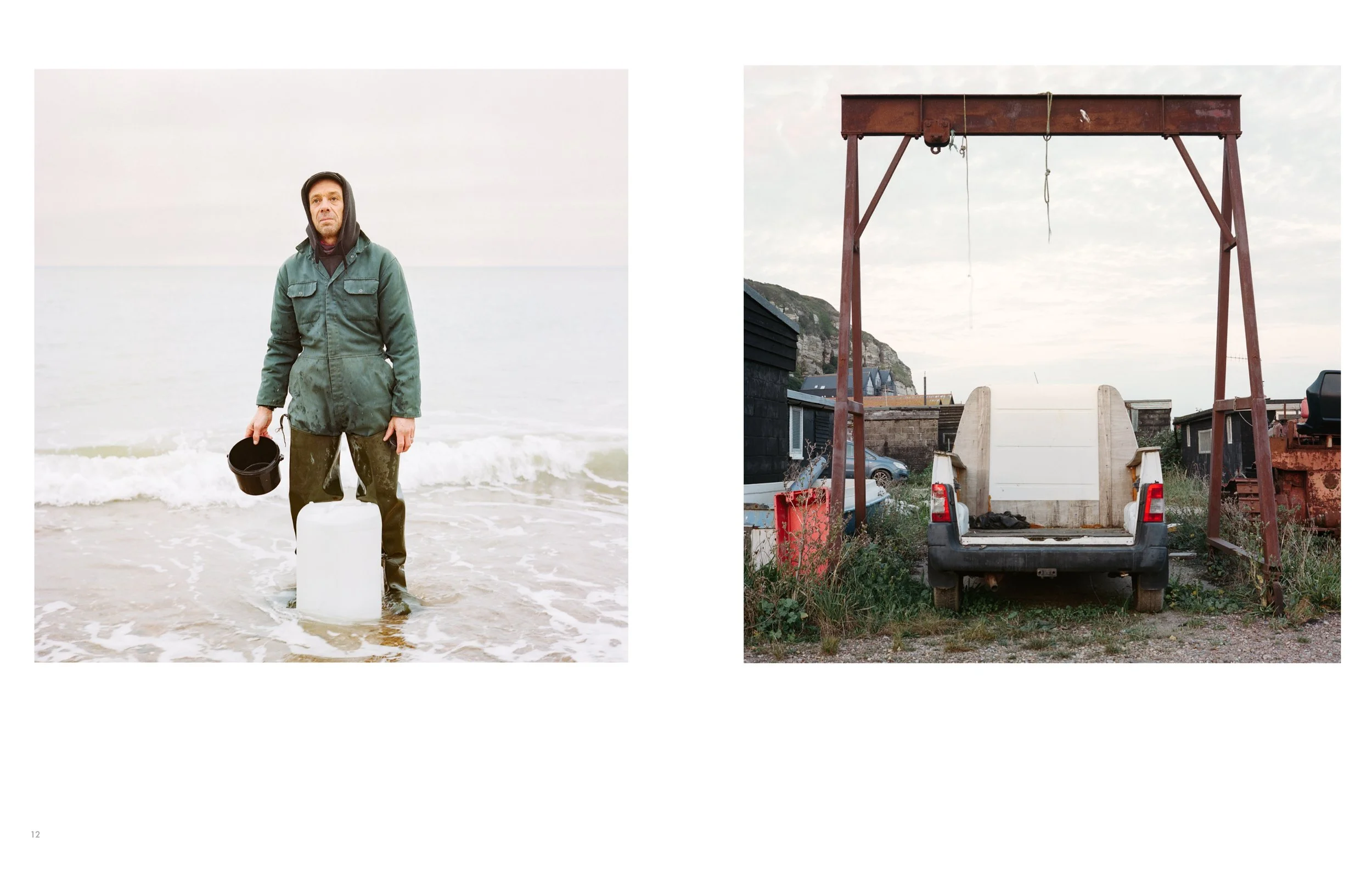 A man in a green jacket with a hood standing in the ocean holding a black bucket, with a white container at his feet, and an overcast sky.