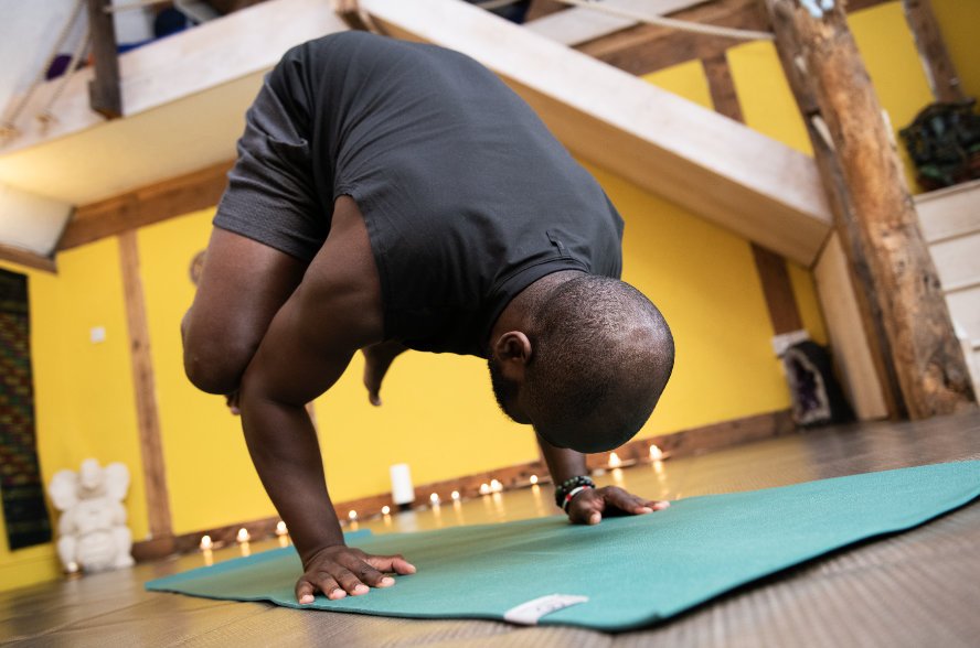 A person practicing yoga in a studio, balancing on their hands with head and body curved downward, on a green yoga mat.