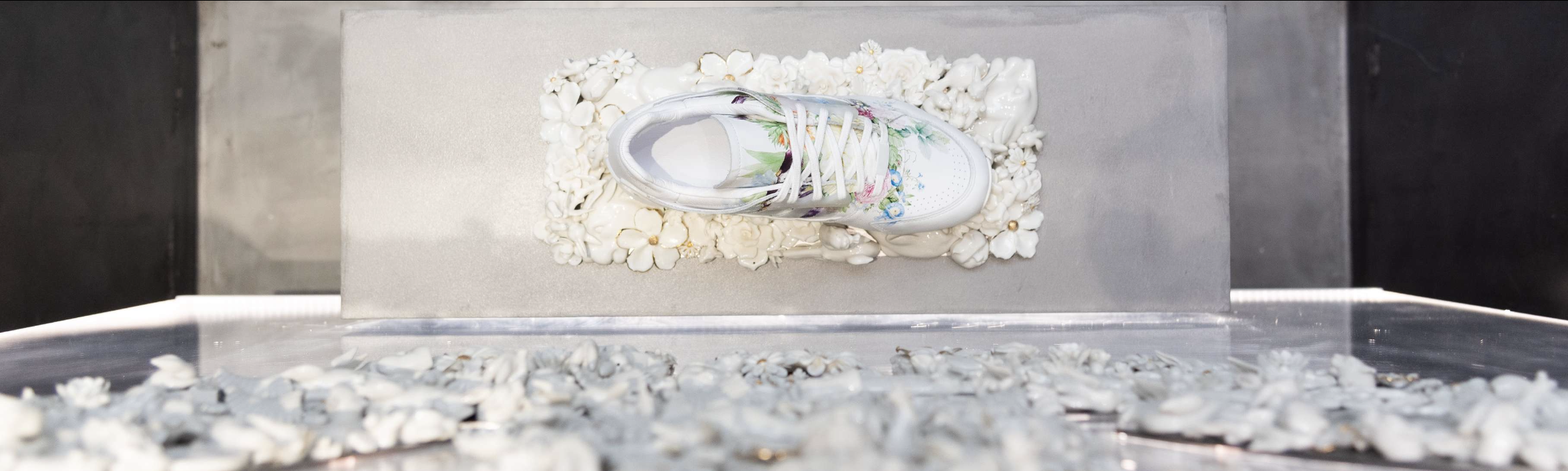White sneaker displayed among white flowers in a sculptural installation.