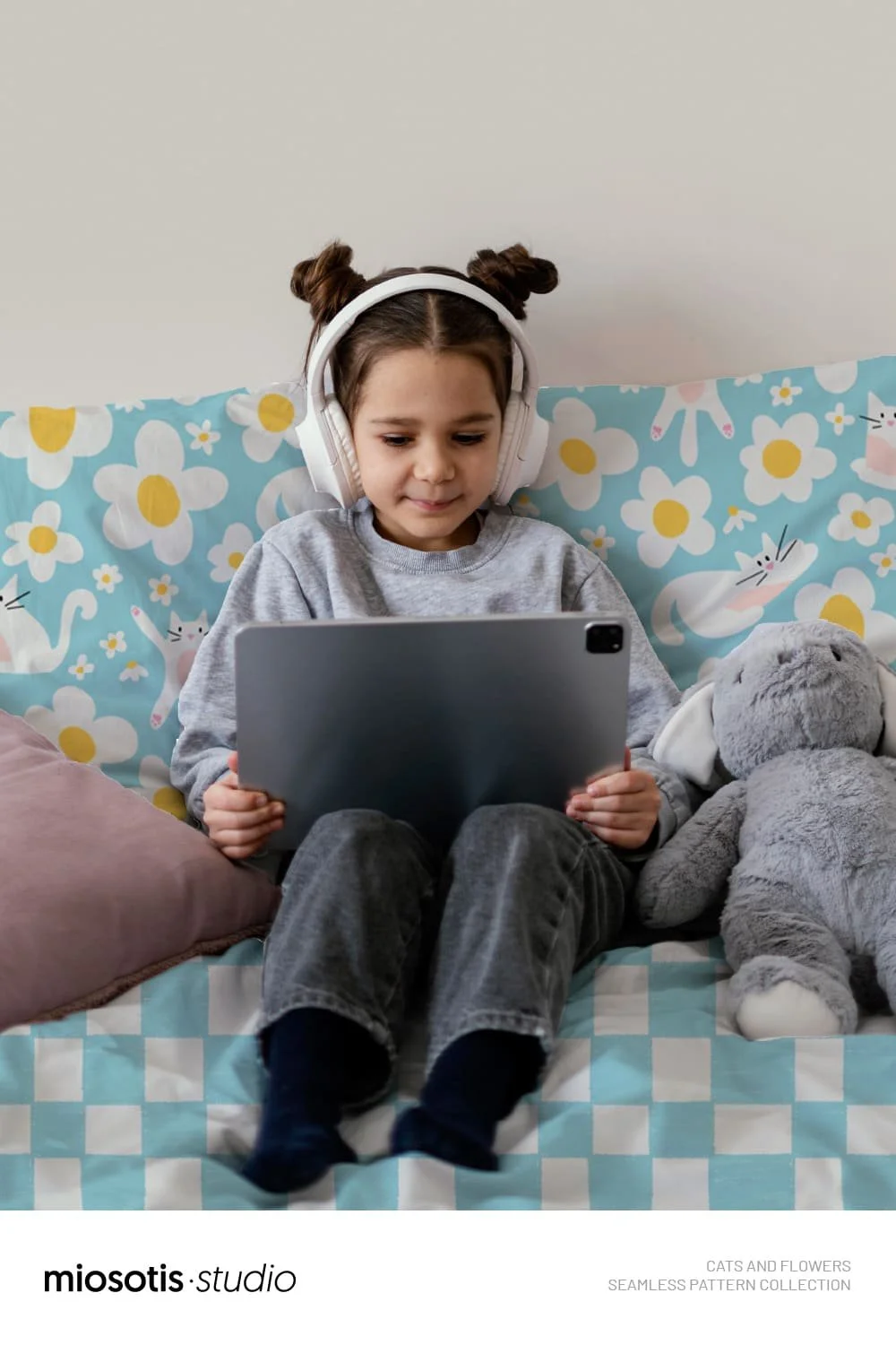 Child relaxing on a bed surrounded by the playful cats and flowers pattern on bedding.