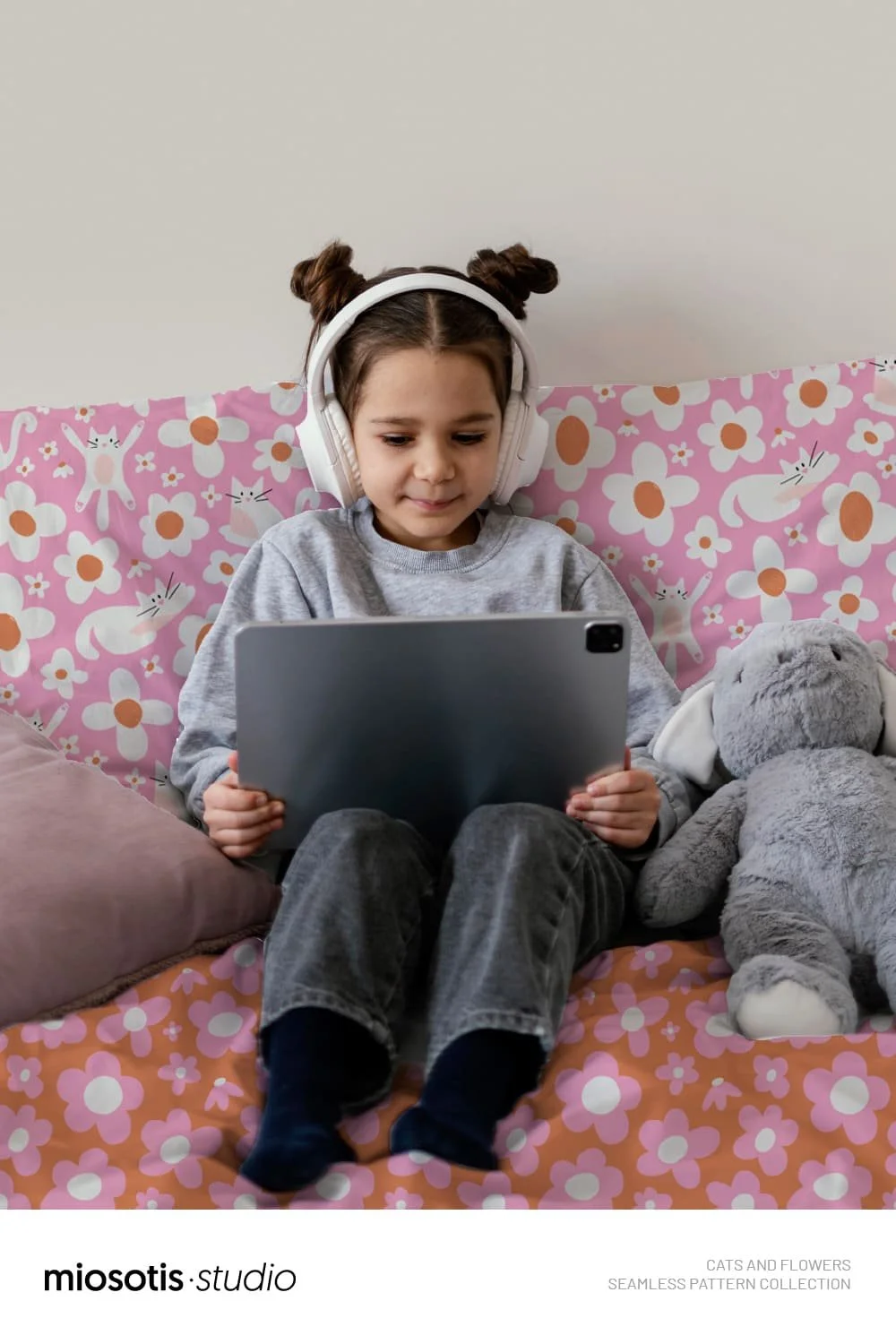 Child relaxing on a bed surrounded by the playful cats and flowers pattern on bedding.