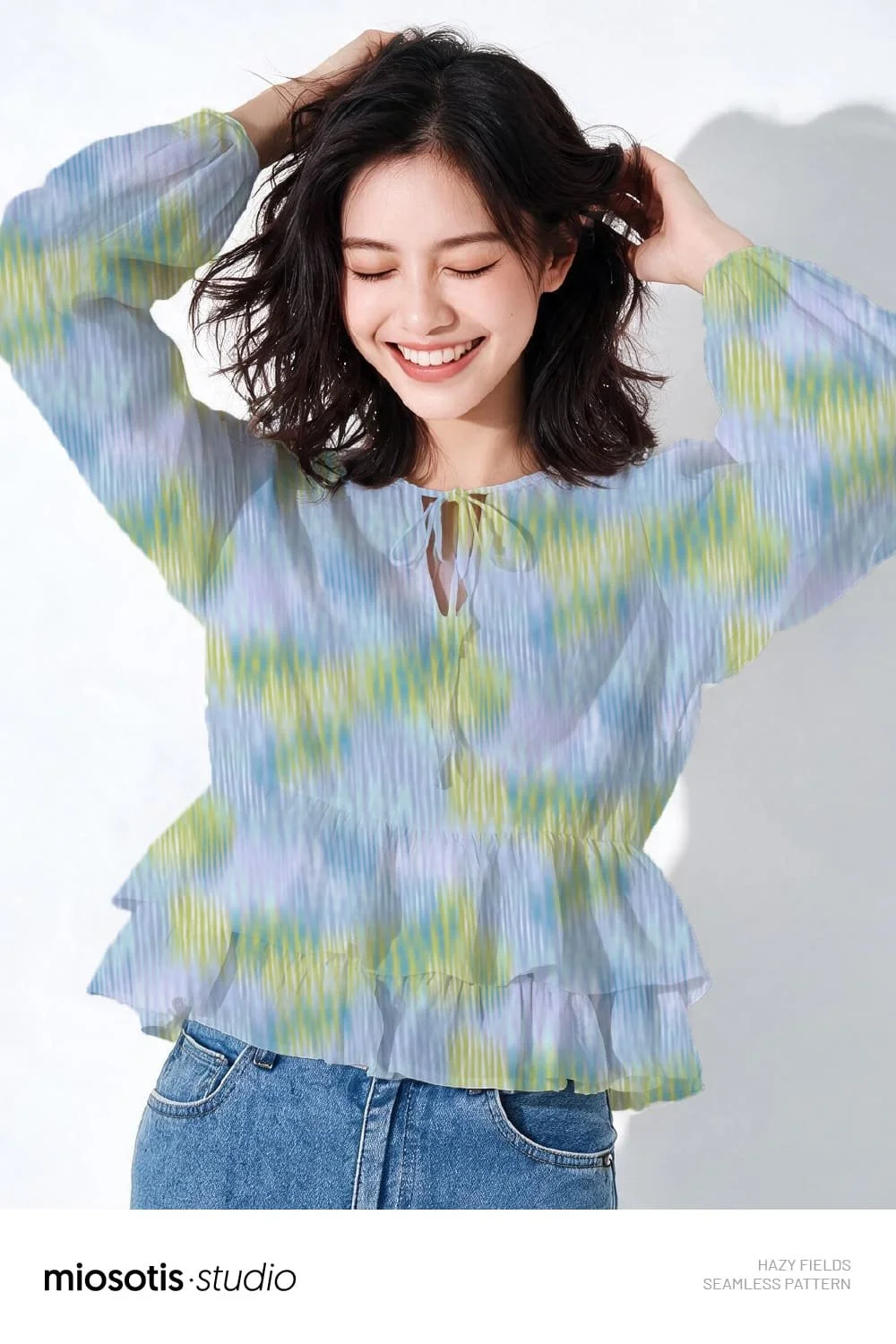 Woman wearing a blouse featuring the Hazy Fields abstract texture pattern in soft green, blue and lilac tones.