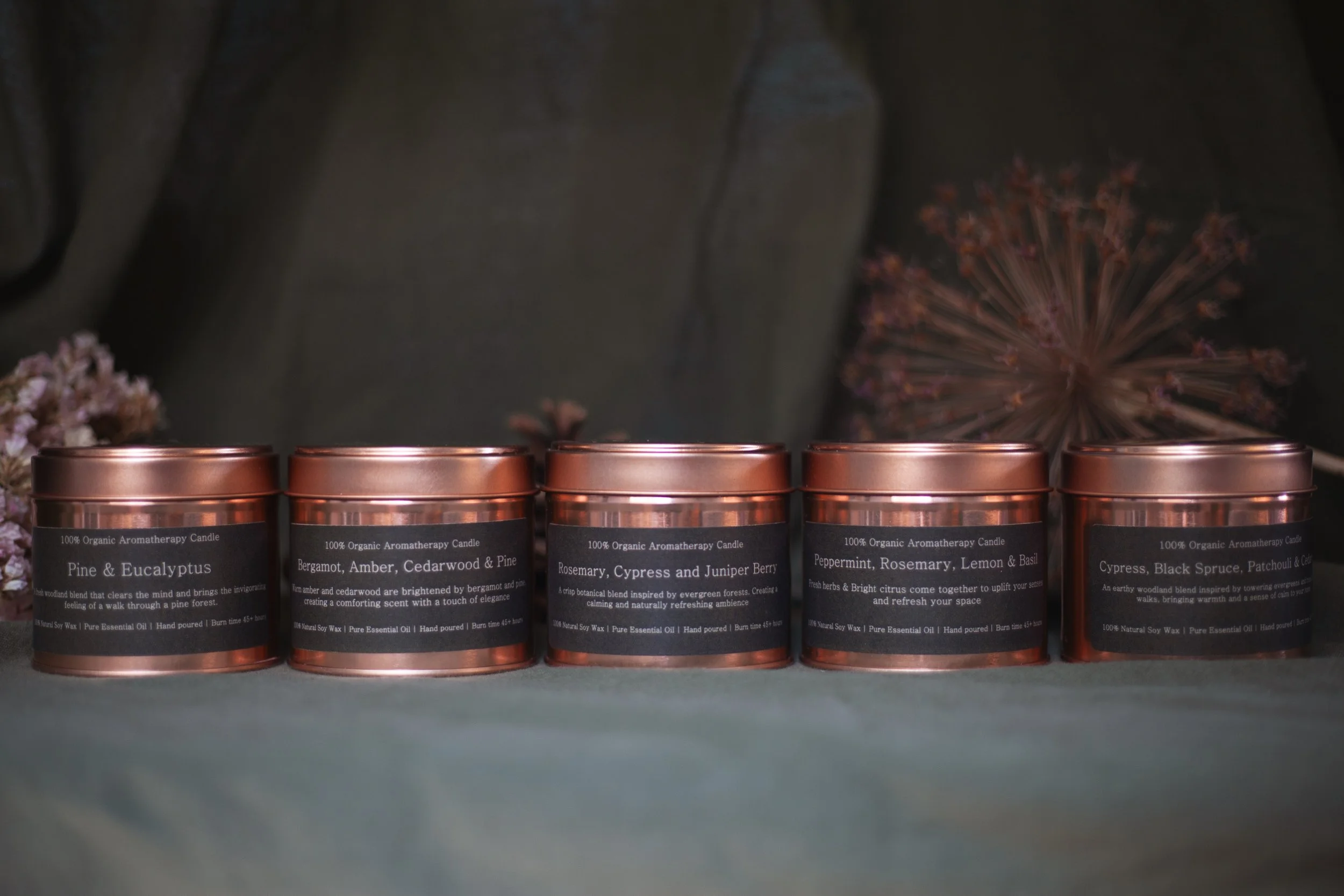 Collection of Bouquets on a Boat organic aromatherapy soy candles in amber glass tins with copper lids, featuring woodland-inspired essential oil fragrances on a dark green natural backdrop.