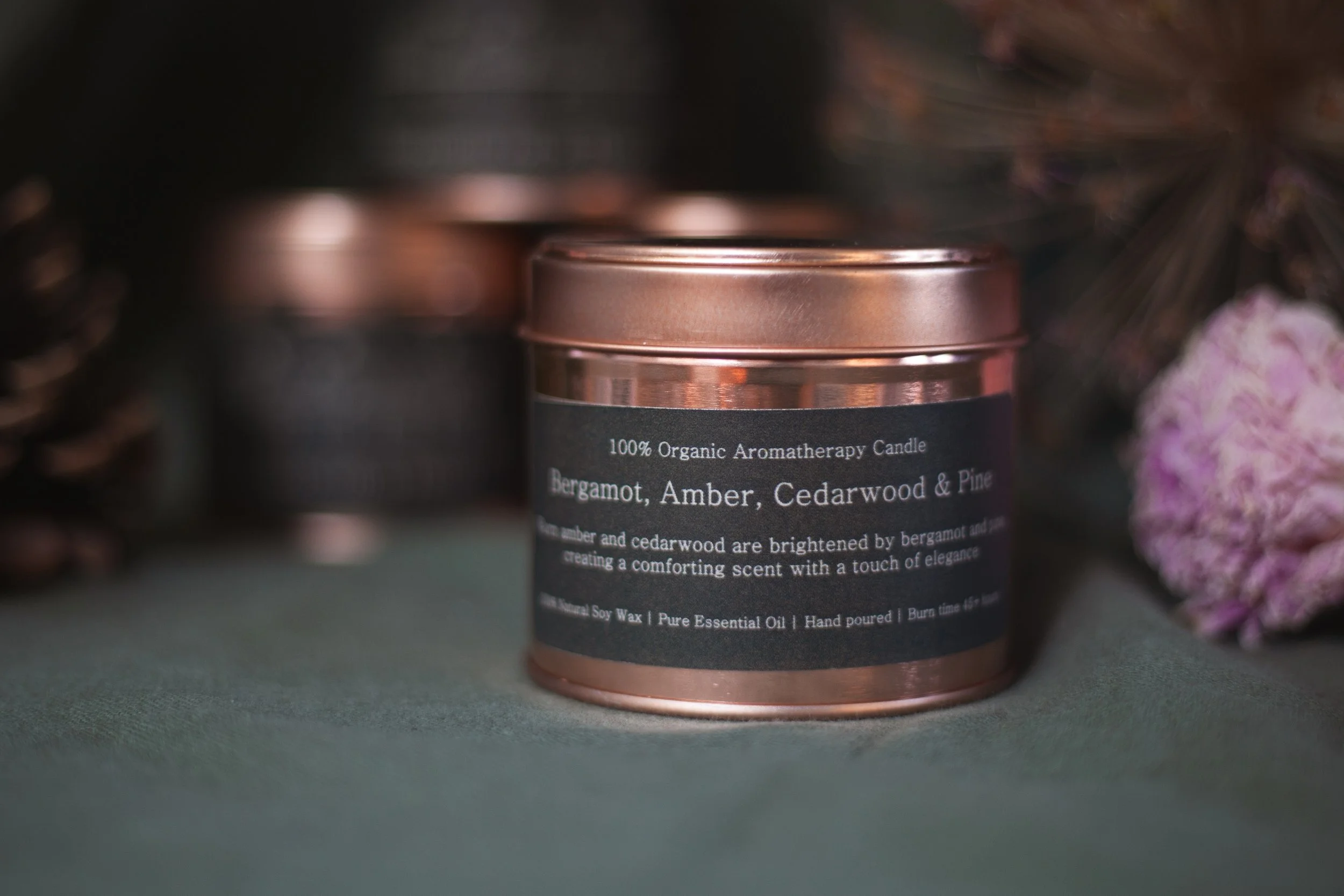 Bergamot, amber, cedar wood and Pine organic aromatherapy soy candle by Bouquets on a Boat in an amber glass jar with a copper lid, styled with pinecones and dried flowers.