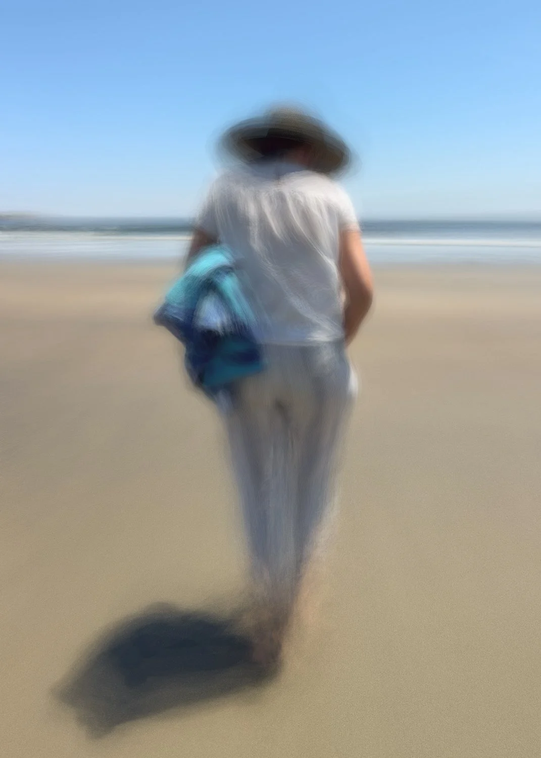 abstract ICM image of a person walking on the beach, wearing a wide-brimmed hat, white shirt, and light-colored pants, carrying a blue towel or blanket, with the ocean and blue sky in the background.