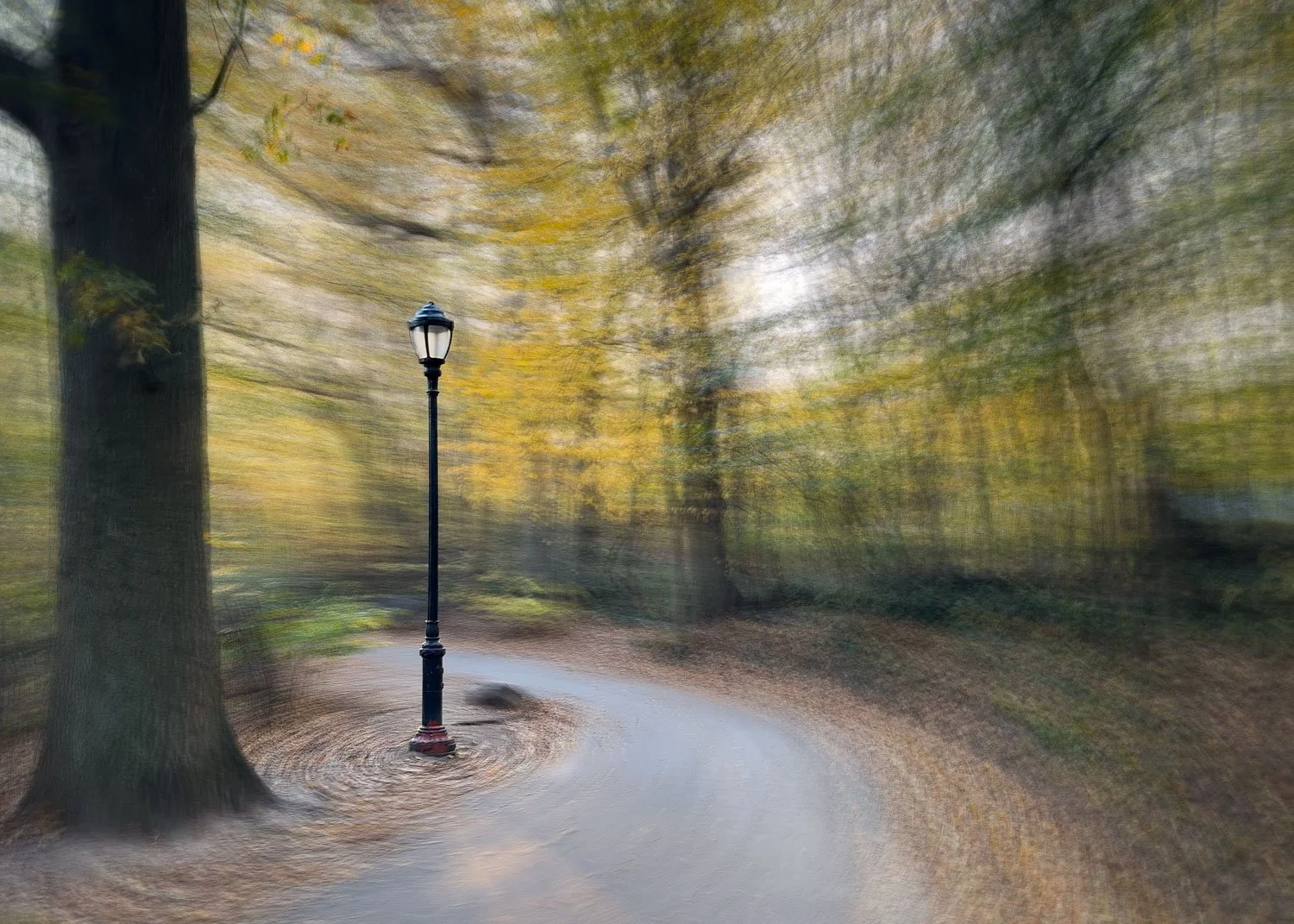Abstract ICM Bluristic  photo - A park with a curved pathway, a black lamppost, large trees with yellow and green leaves, and a blurred background creating a swirling effect.