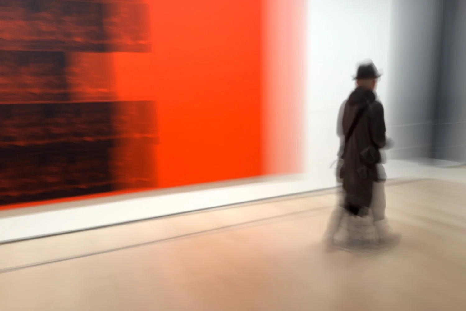 Abstract ICM Bluristic  photo - Person walking through an art gallery with abstract orange and black artwork on the wall.