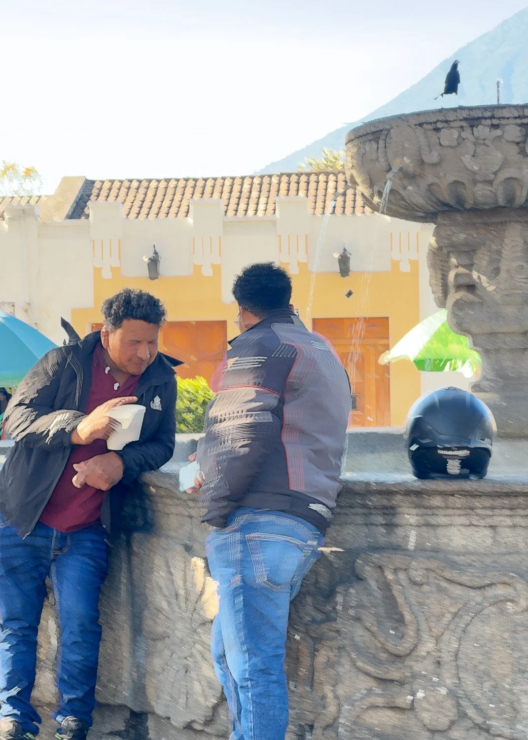 Abstract ICM Bluristic  photo - Two men are standing and talking at a stone fountain in an outdoor plaza with a building and mountain in the background.